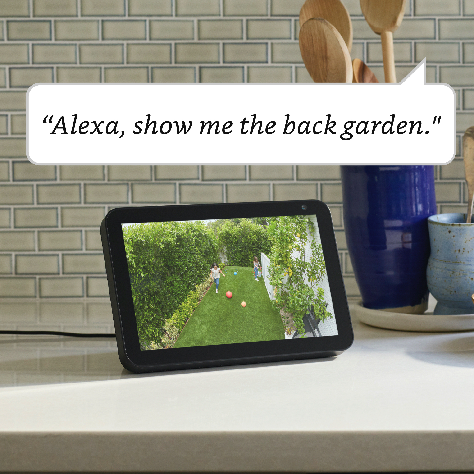 Pantalla inteligente en una encimera. La pantalla muestra un jardín trasero con niños jugando. Texto.