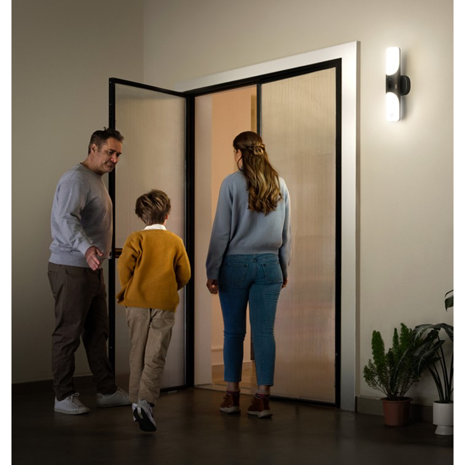 Rodzina wchodząca do domu, widziana z zewnątrz. Drzwi wejściowe są otwarte.