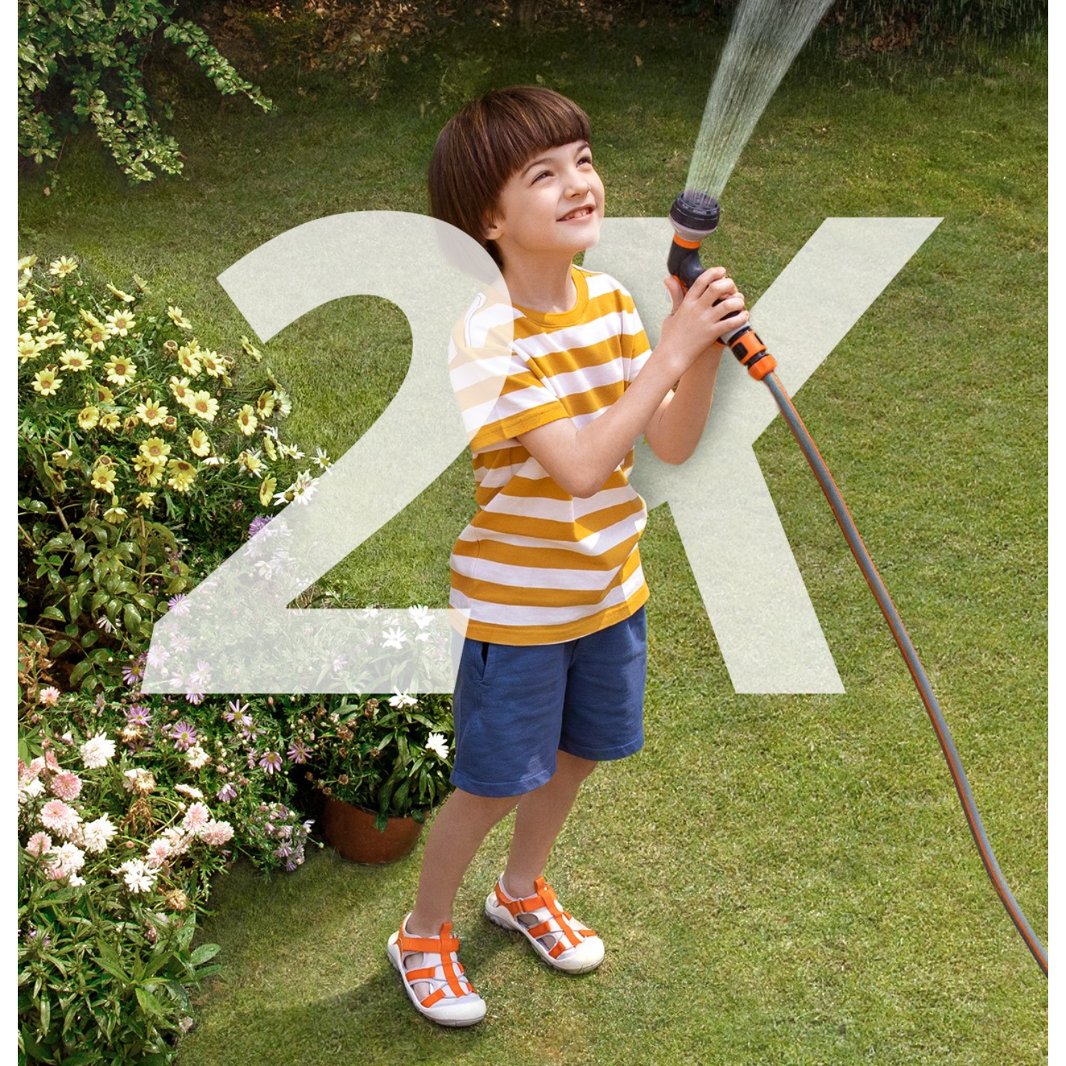 Chłopiec w pasiastym t-shircie podlewa trawnik wężem. Jest grafika 2X.