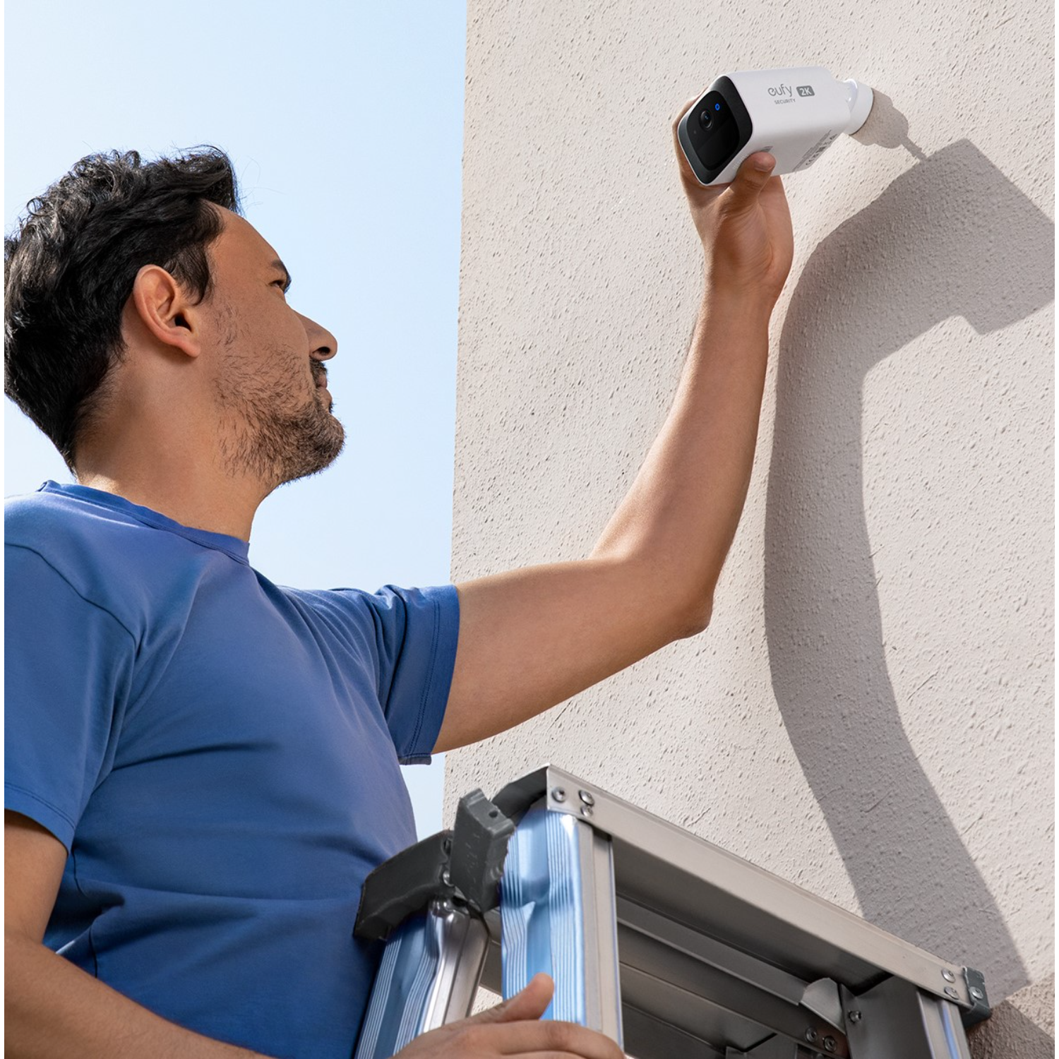 Mężczyzna na drabinie instaluje białą kamerę bezpieczeństwa na ścianie.
