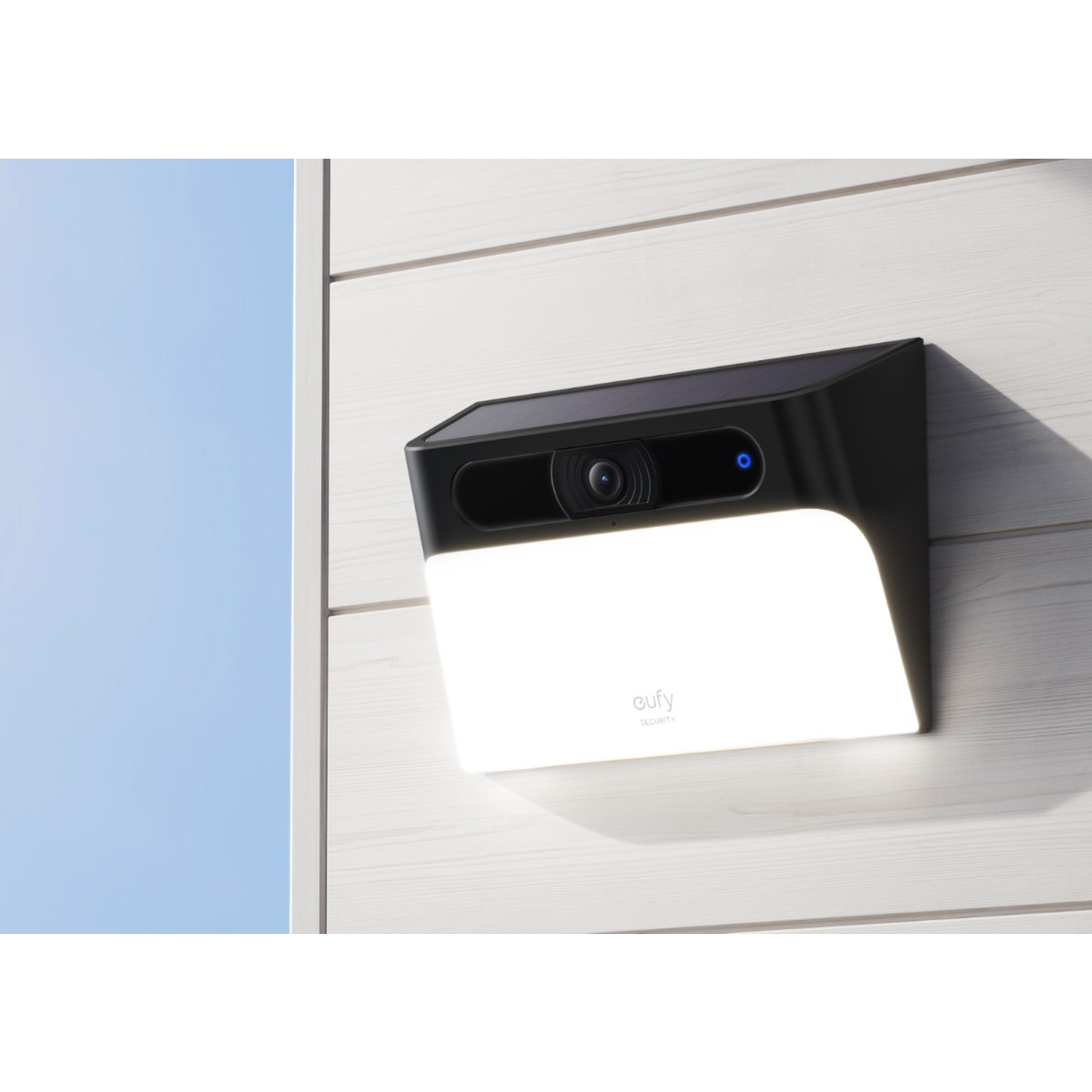 Czarna kamera bezpieczeństwa ze światłem zamontowanym na białej ścianie. Niebo jest niebieskie.