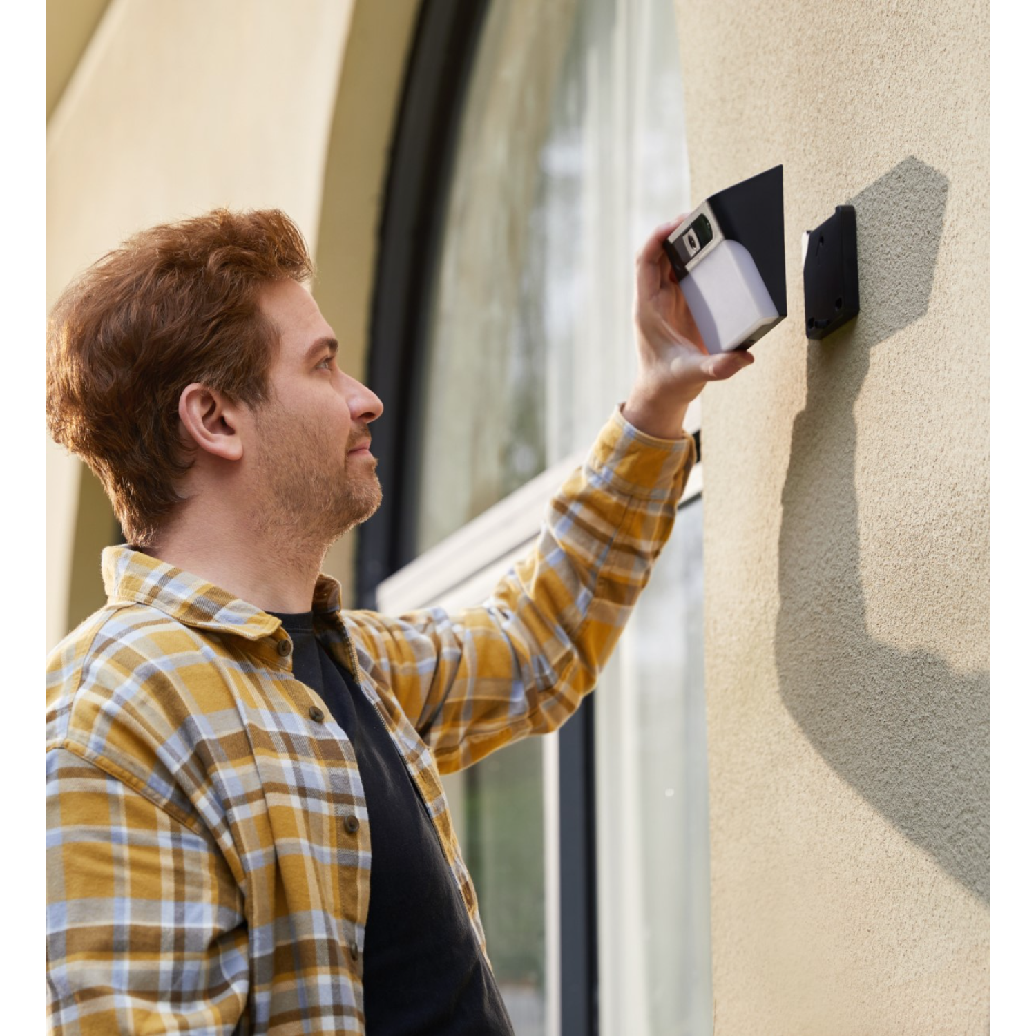 Mężczyzna instaluje białą kamerę bezpieczeństwa na beżowej ścianie. Kamera jest czarno-biała.