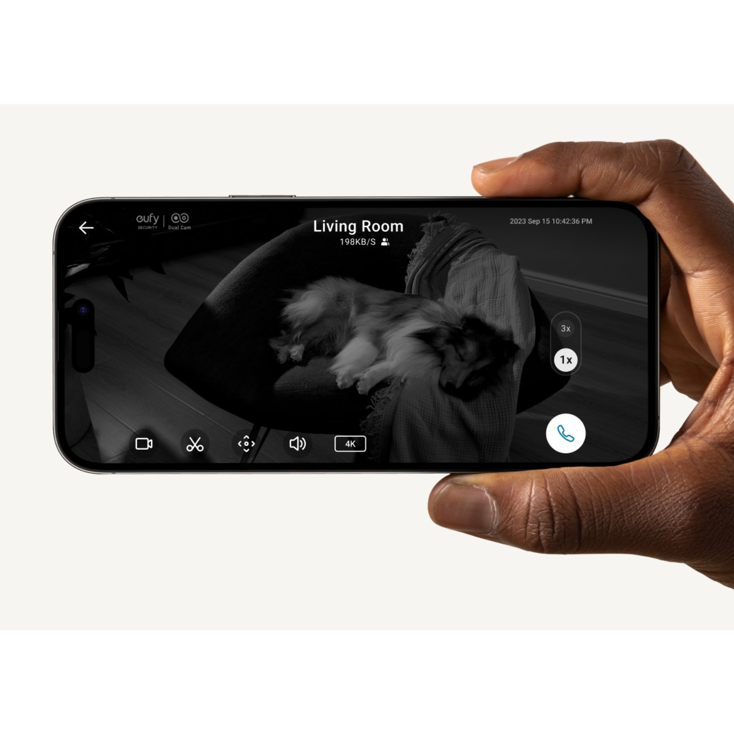 Ręka trzymająca telefon z widokiem salonu. Pies na kanapie, wiele ikon kontrolnych.