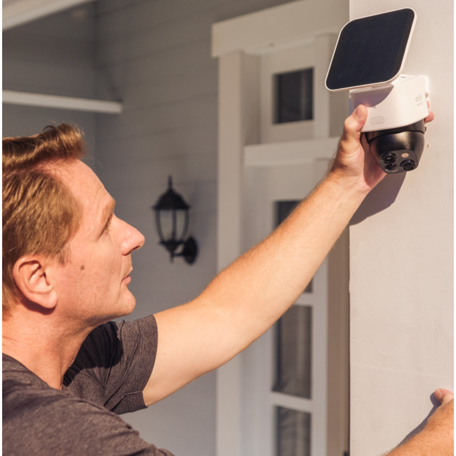Mężczyzna instaluje białą kamerę bezpieczeństwa z panelem słonecznym na białej ścianie.