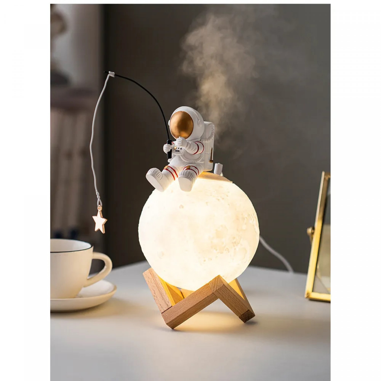 Astronautenfigur auf einer mondförmigen Lampe, mit Stern und Tasse auf dem Tisch.