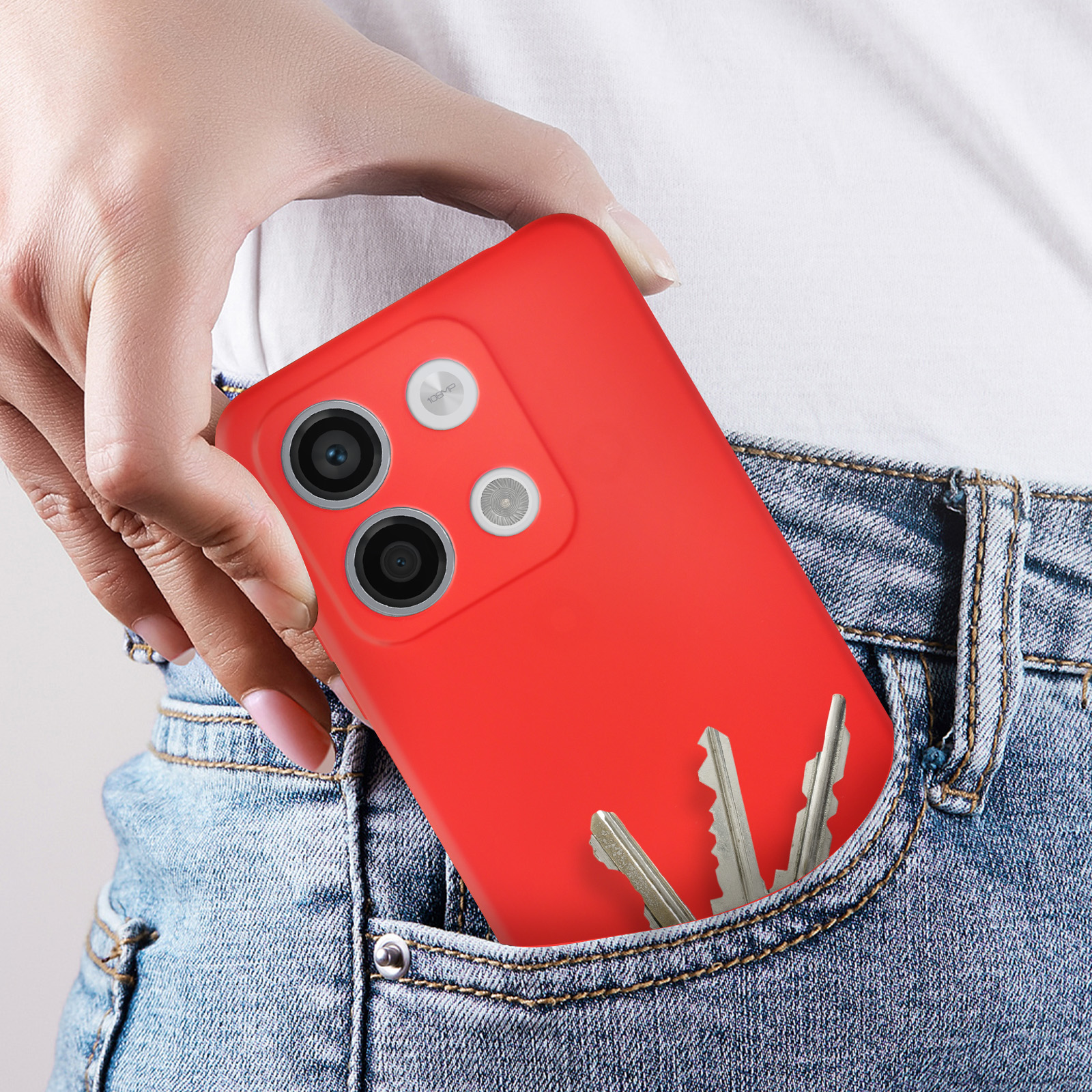 Una mano in una tasca dei jeans tiene un telefono rosso. Le chiavi sono visibili nella stessa tasca.