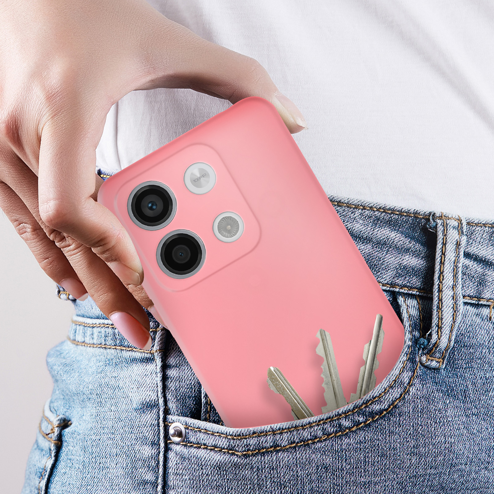 Uno smartphone rosa in una tasca di jeans, tenuto da una mano. Anche le chiavi sono in tasca.