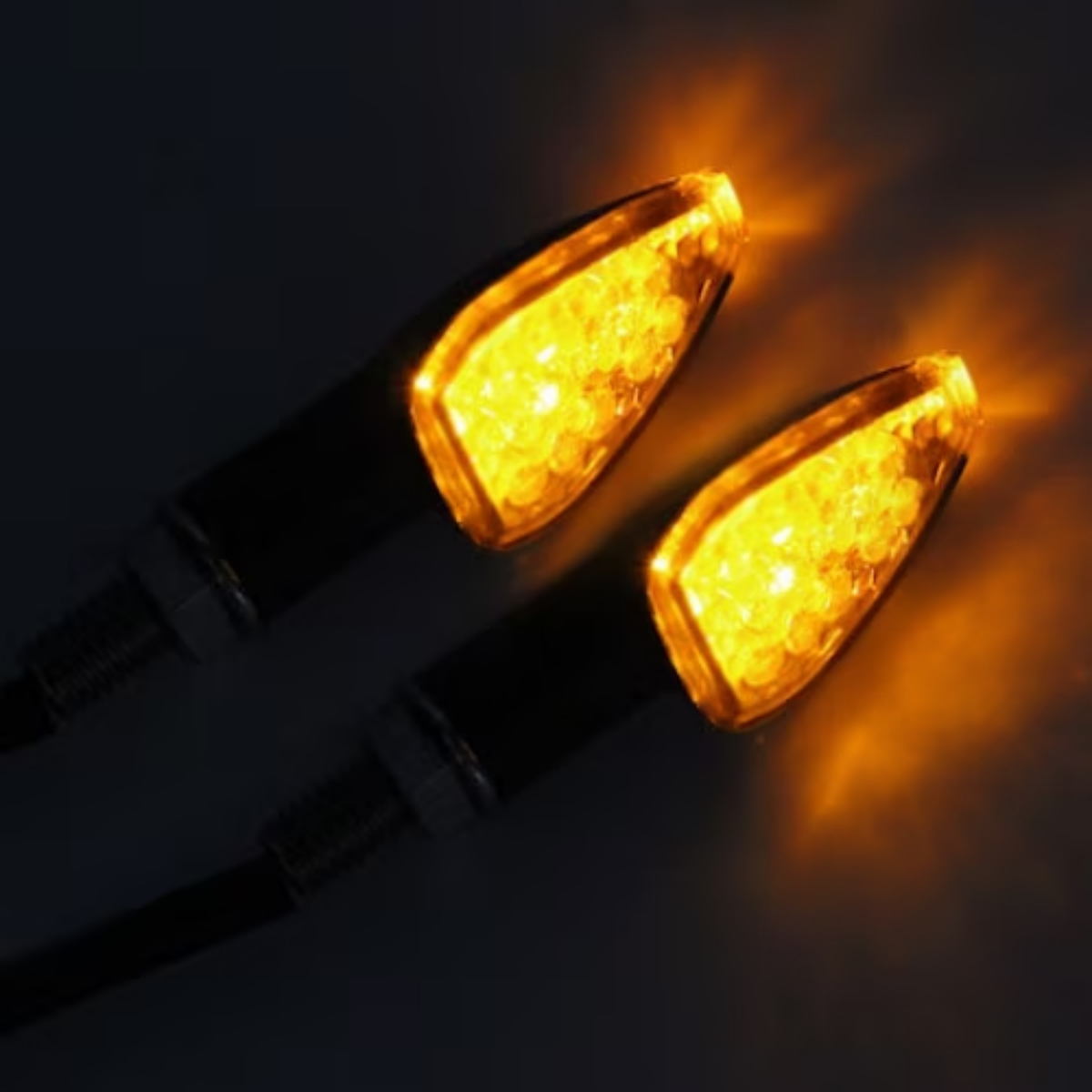 Zwei beleuchtete orangefarbene Blinker mit schwarzen Stielen, vor dunklem Hintergrund.