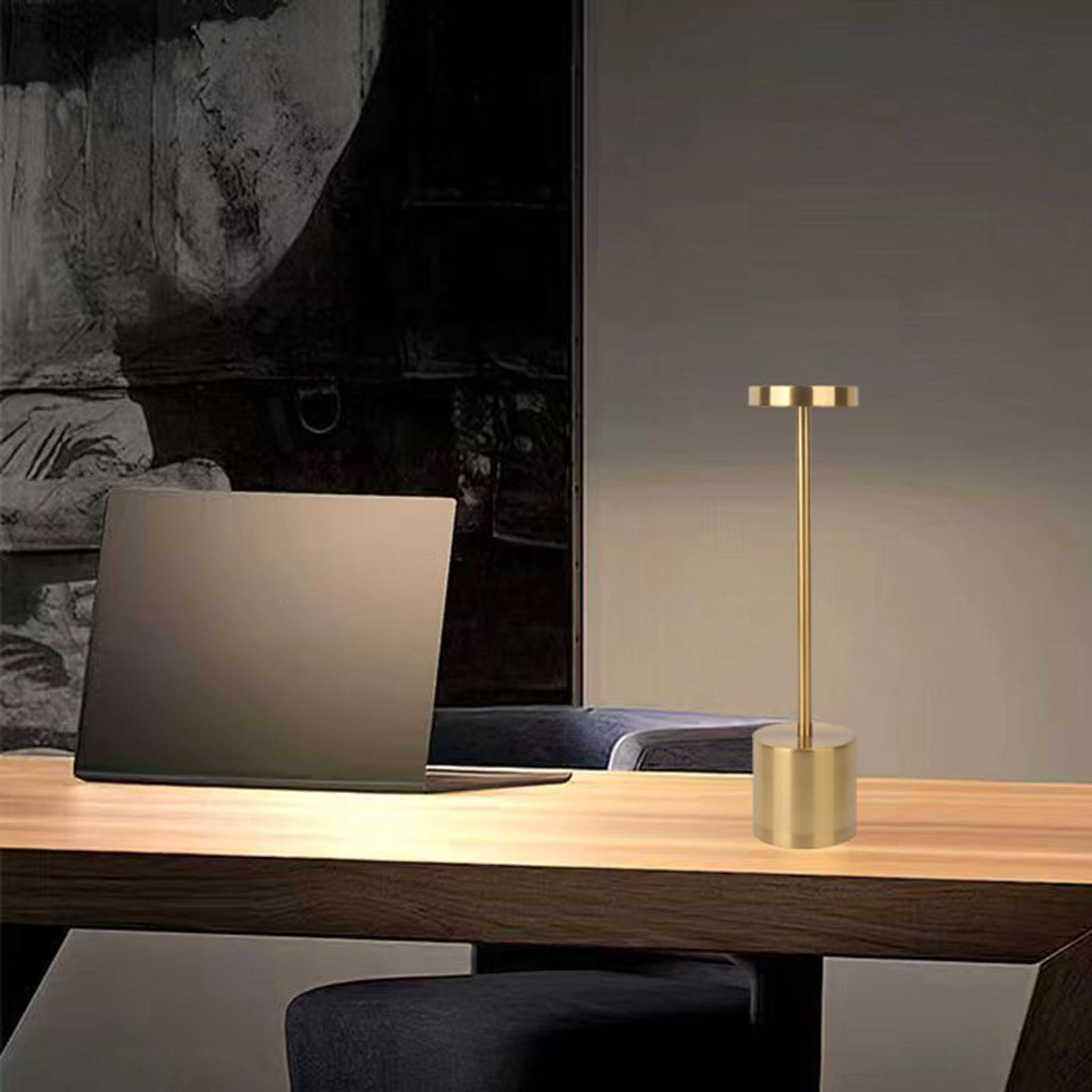 Goldene Tischlampe auf Holztisch, mit Laptop und dunklem Hintergrund. Die Lampe ist an.