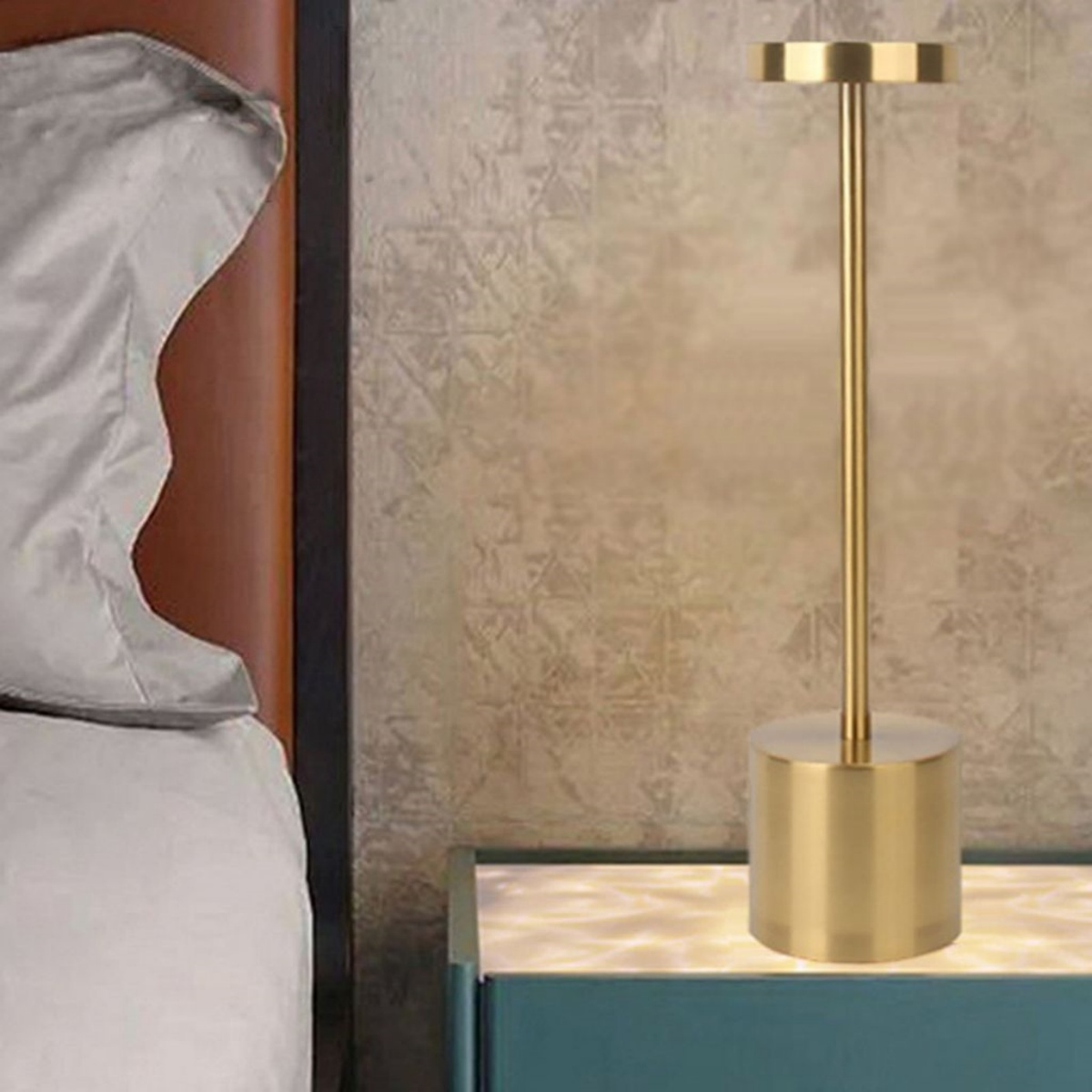 Eine goldfarbene Nachttischlampe. Die Lampe hat einen zylindrischen Fuß und einen hohen, geraden Stiel.