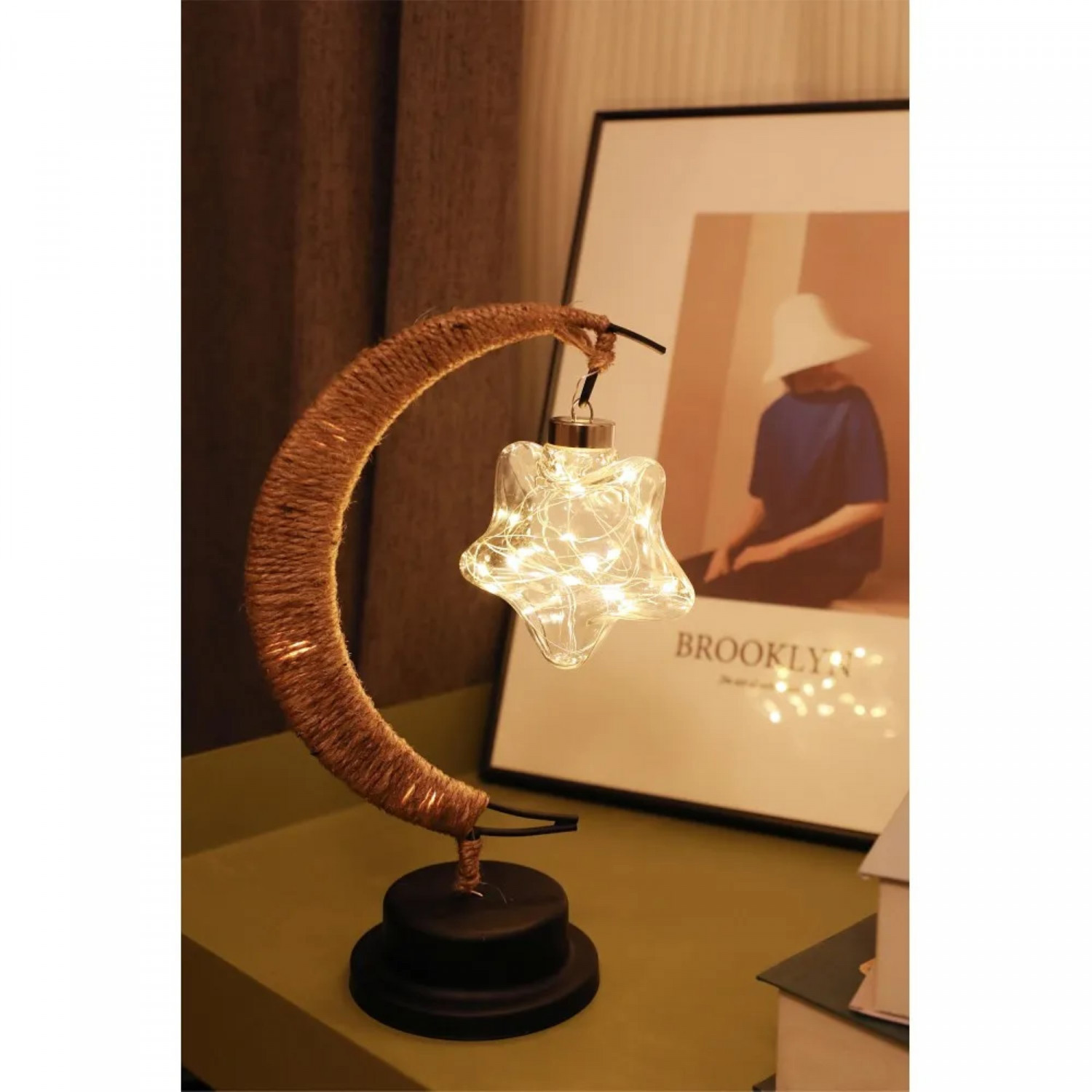 Eine sternförmige Lampe mit Lichtern im Inneren, die an einem sichelförmigen Rahmen hängt. Im Hintergrund ein Bild.