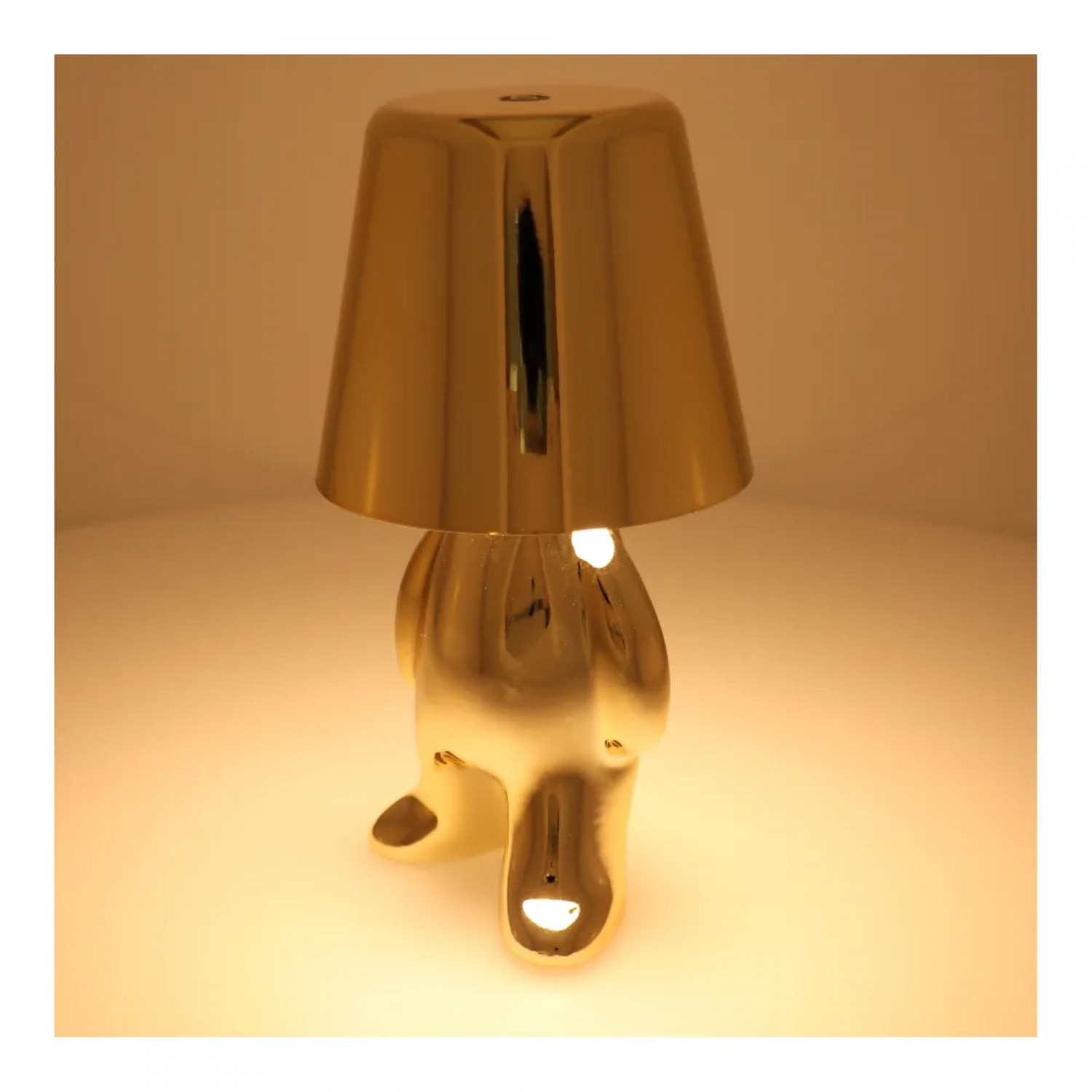 Goldfarbene Lampe in Form einer Person. Sie hat einen Lampenschirm oben drauf.