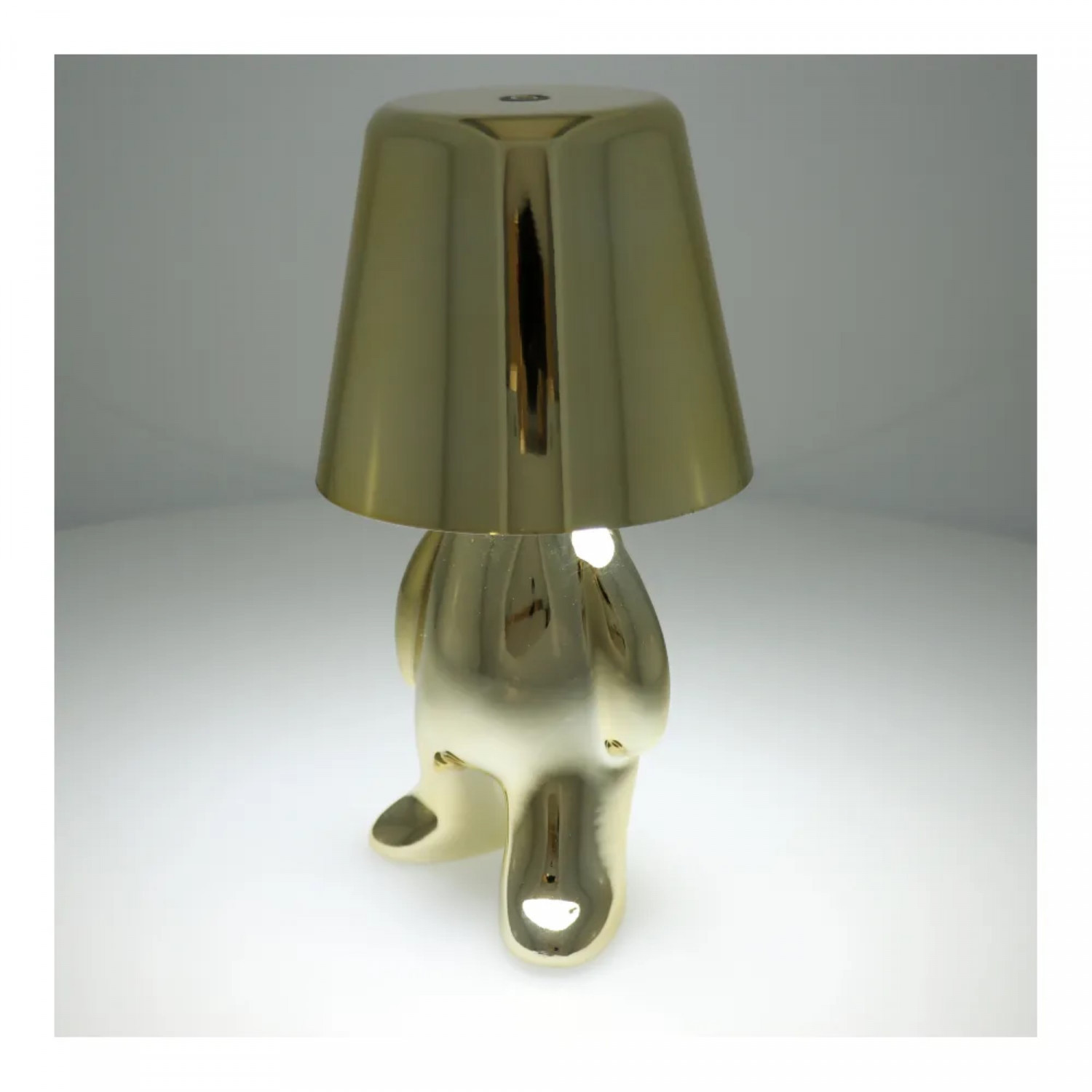 Goldfarbene Lampe mit figurartigem Sockel in Form einer Person mit Lampenschirm auf dem Kopf.
