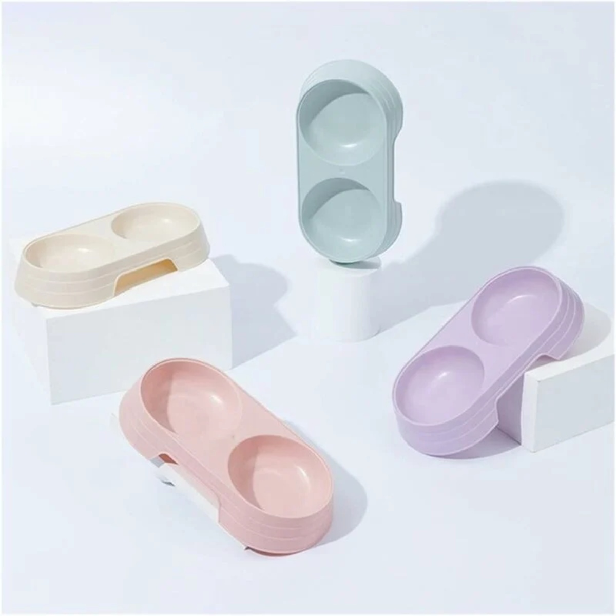 Vier Futternäpfe für Haustiere in verschiedenen Farben: beige, grün, rosa und lila auf weißen Podesten.