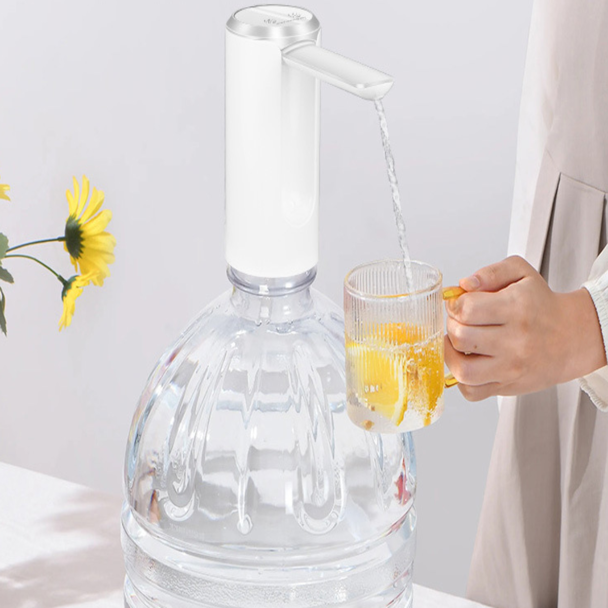 Ein Wasserspender mit weißem Oberteil und einer durchsichtigen Plastikwasserflasche. Eine Person gießt Wasser in ein Glas.