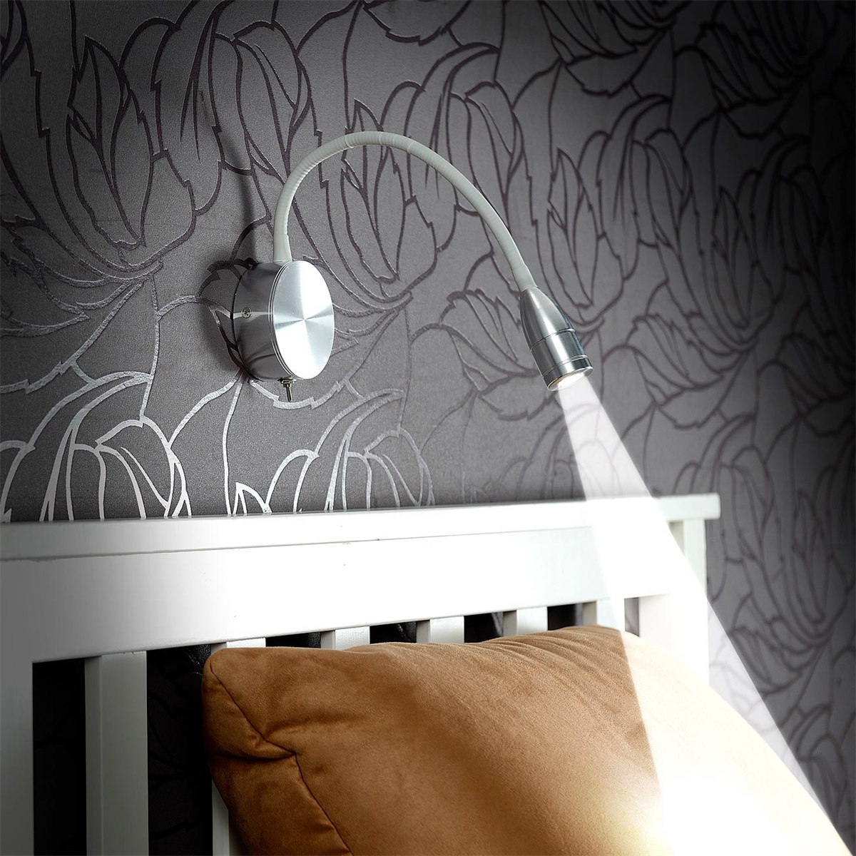 Wandmontierte Leselampe über einem Bett. Das Licht ist silberfarben und auf ein braunes Kissen gerichtet.
