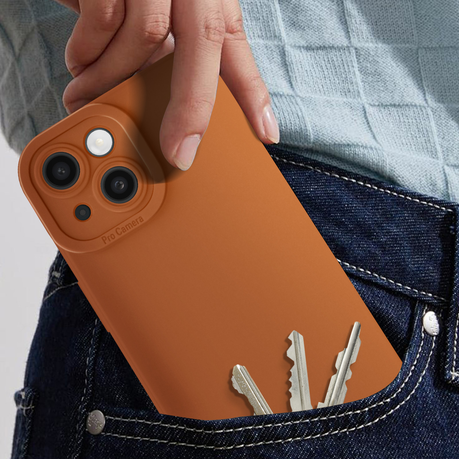 Mano in tasca dei jeans che tiene un telefono marrone, con chiavi, primo piano, su sfondo bianco.