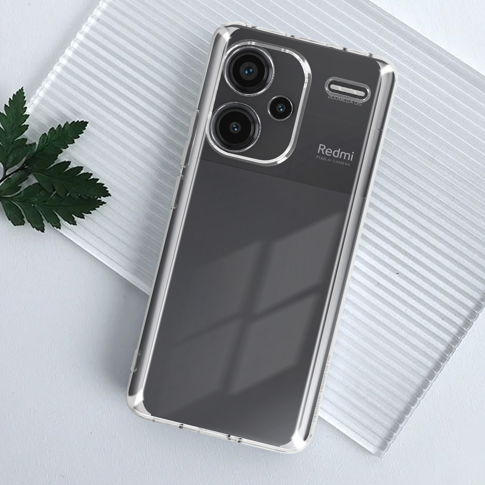 Telefono con fotocamera e custodia trasparente su una superficie bianca con una foglia.
