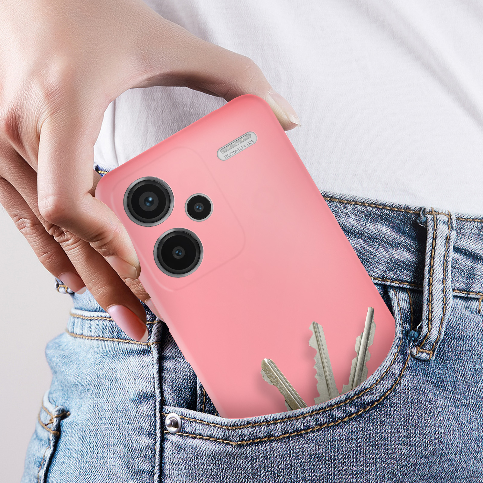 Mano sosteniendo una funda de teléfono rosa con llaves en el bolsillo. Bolsillo de jeans, camisa blanca.