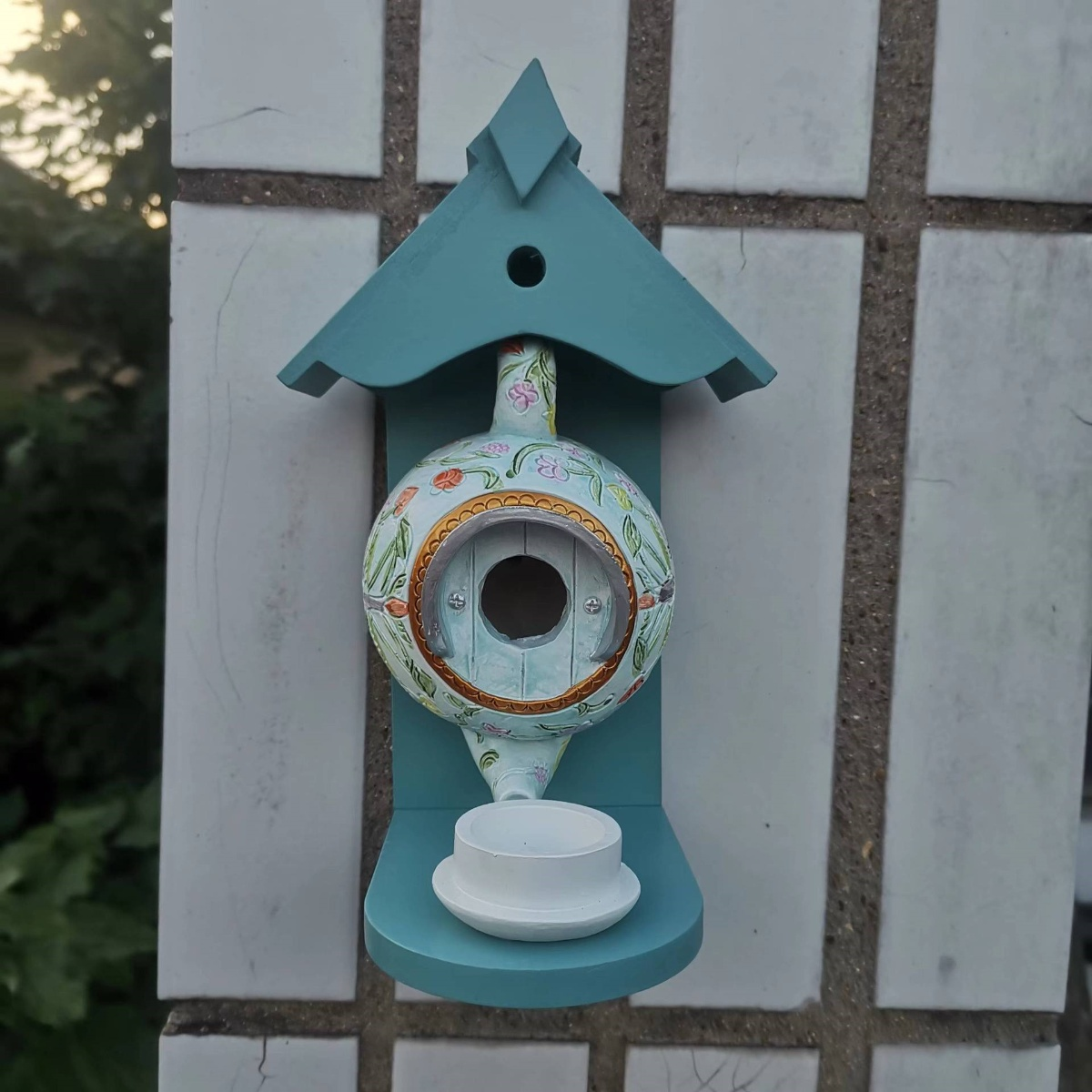 Türkisfarbenes Vogelhaus an weißer Kachelwand, mit Holztablett.