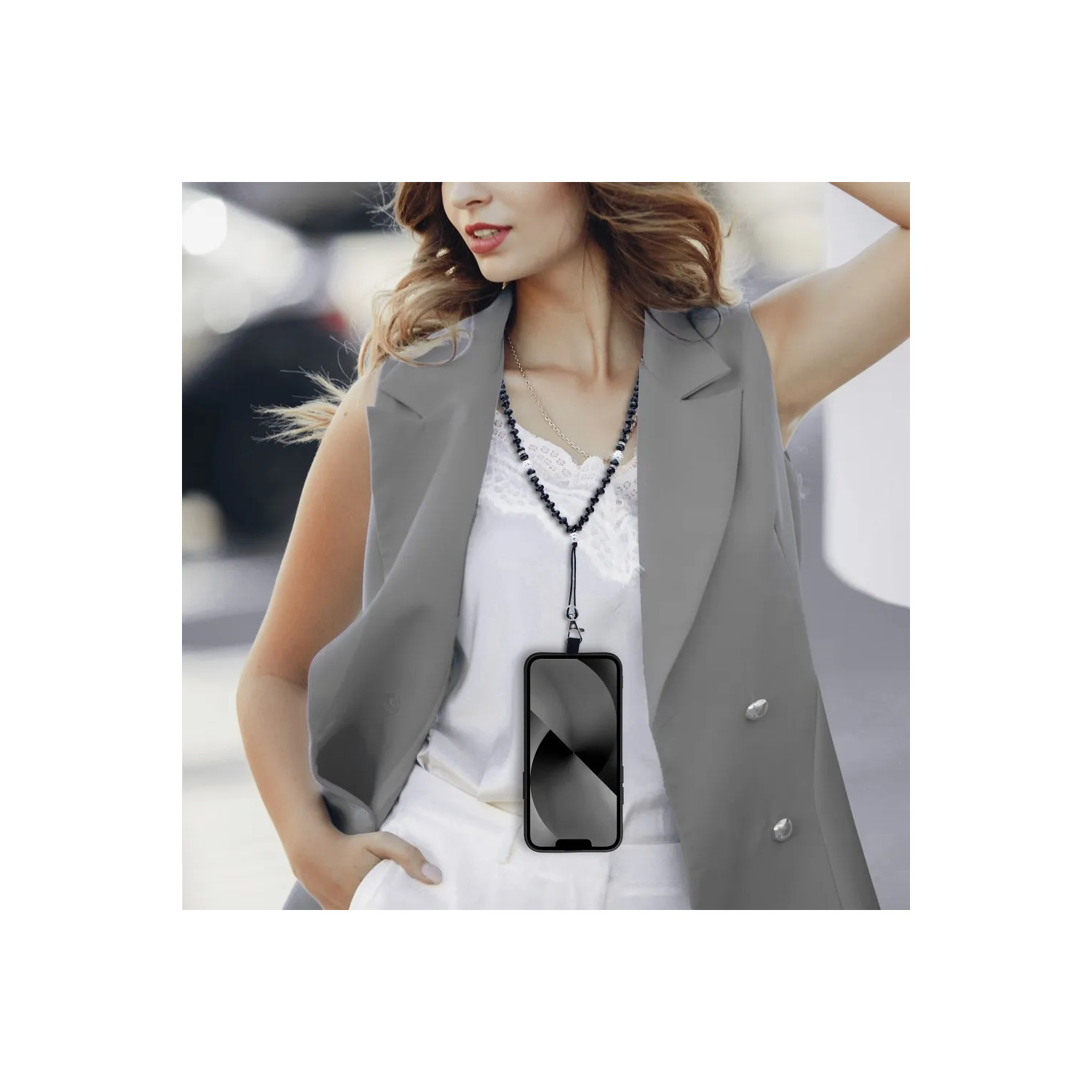 Una donna con un gilet grigio, tiene un telefono con una collana. Il telefono ha uno schermo nero.
