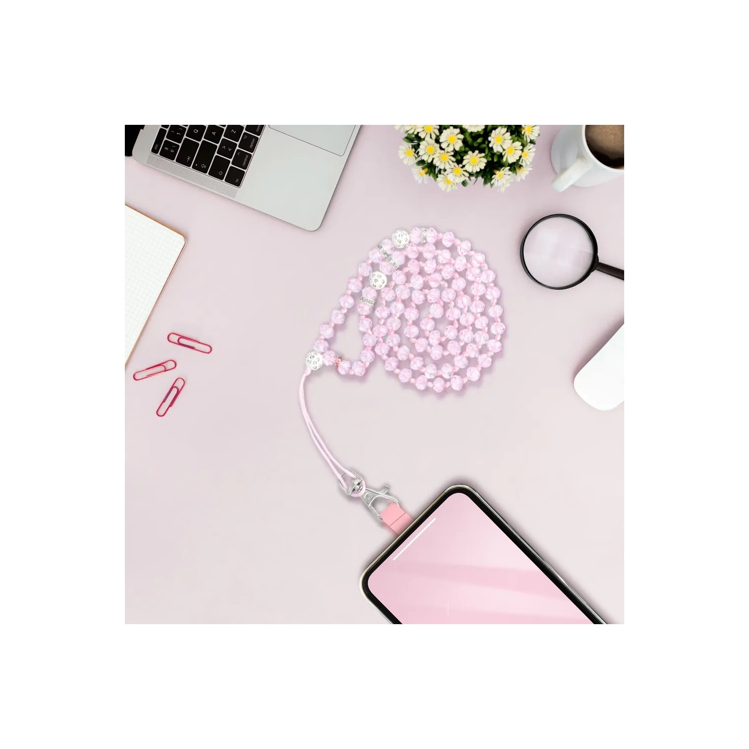 Arbeitsbereich mit Telefon, Perlen, Laptop, Lupe und Blumen. Rosa Oberfläche.