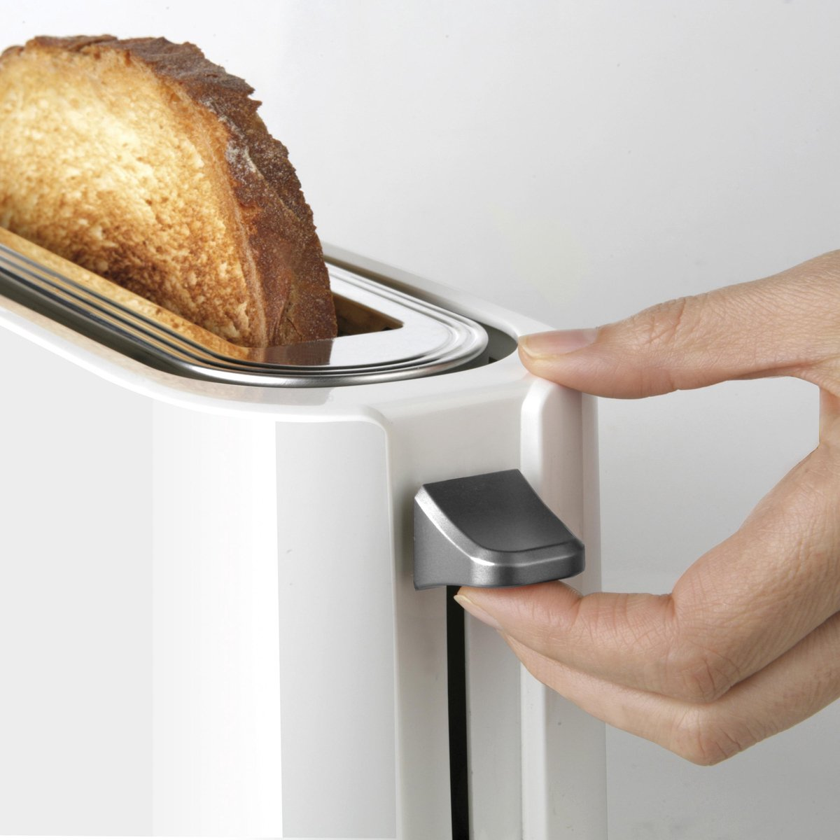 Dłoń naciska dźwignię w białym tosterze. W środku znajduje się kawałek tost.