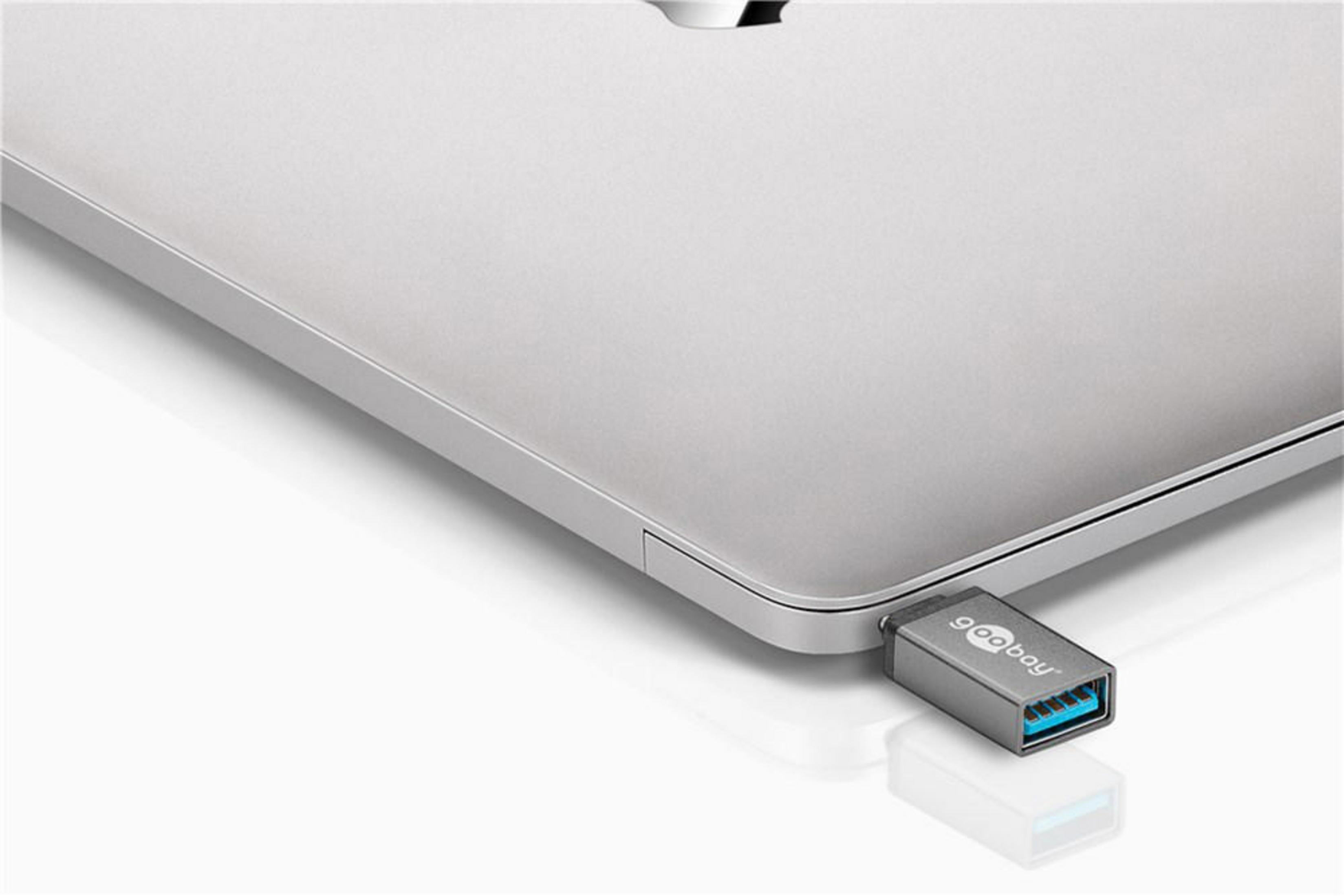 Un adattatore USB-C è collegato a un laptop argentato. L'adattatore è grigio con un'estremità USB blu.