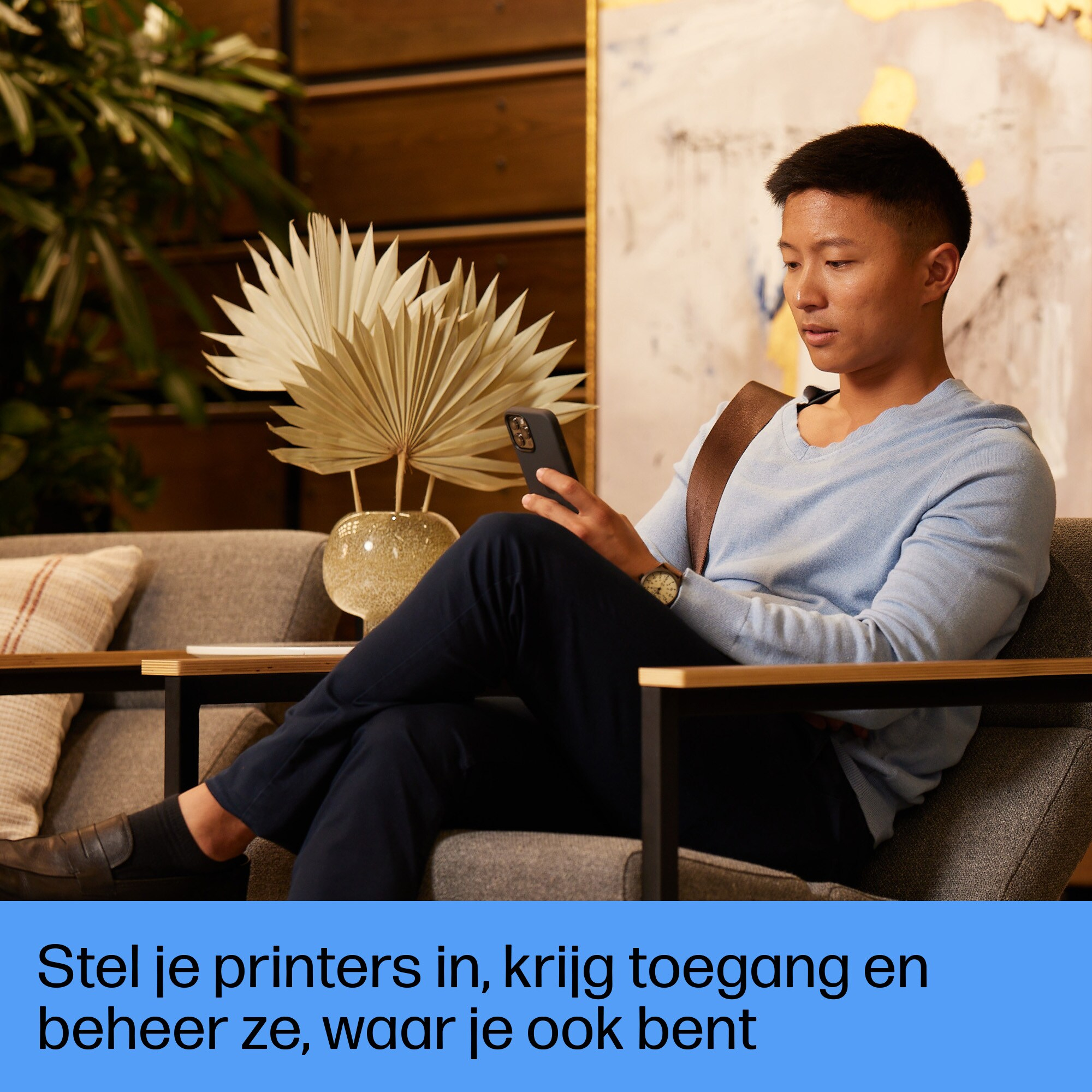 Mężczyzna siedzący na kanapie przegląda telefon. Tekst: 'Zarządzaj drukarkami'.