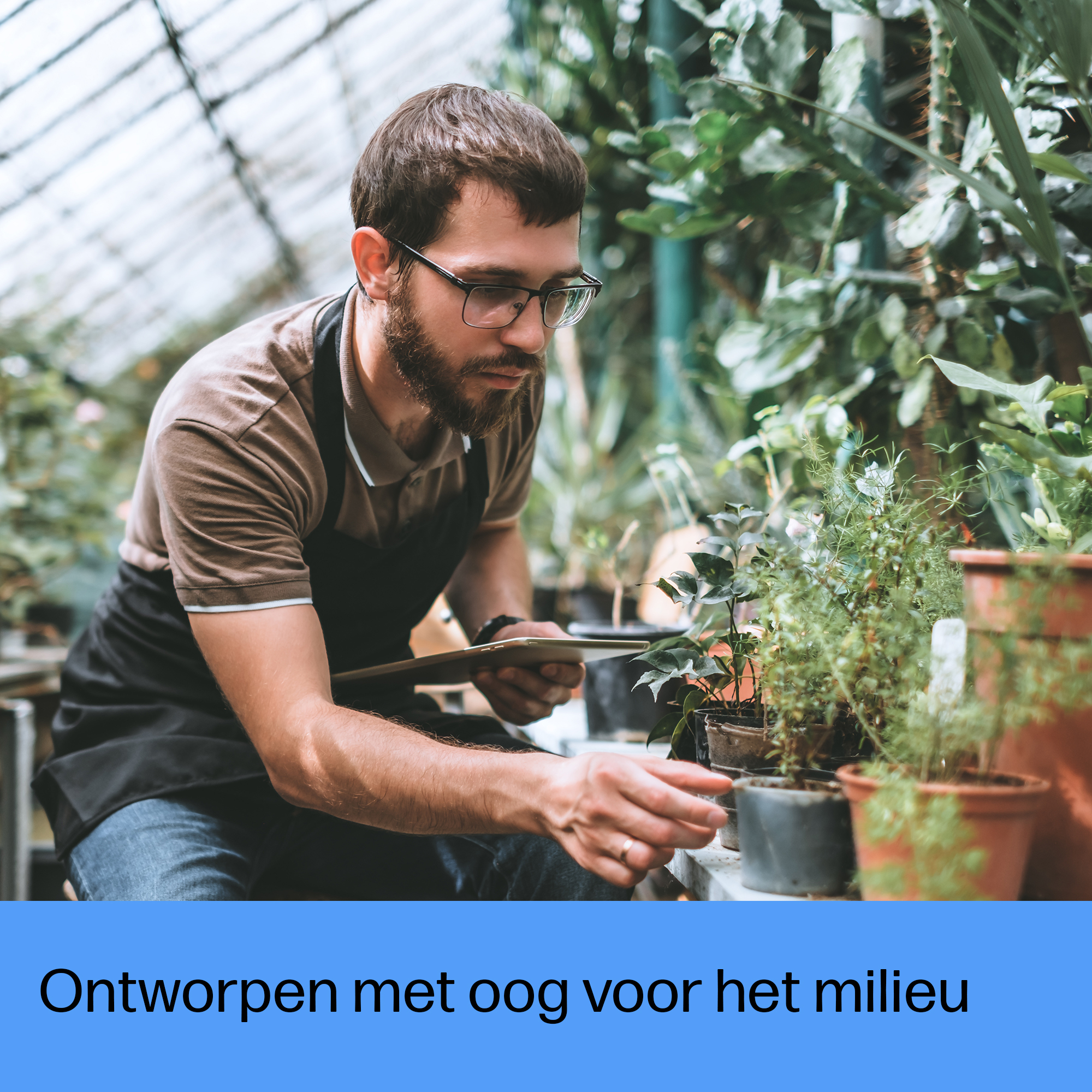 Mężczyzna w szklarni pielęgnujący rośliny. Ma czarny fartuch i okulary, otoczony zielenią.