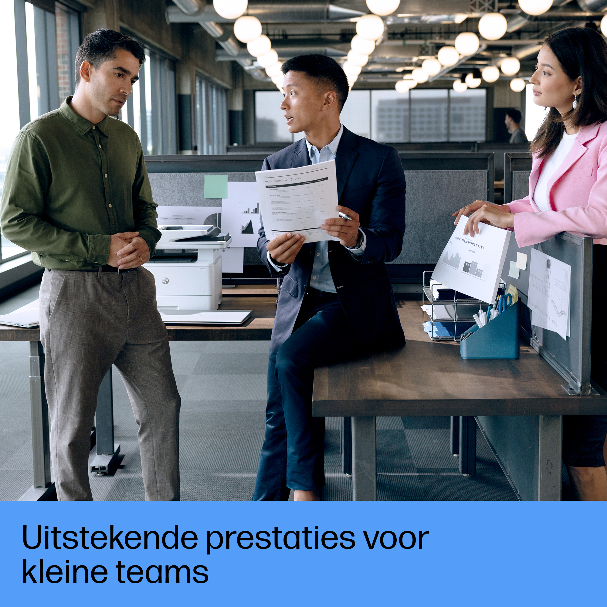 Trzy osoby w biurze, dwie stojące i jedna siedząca. Drukarka w tle.