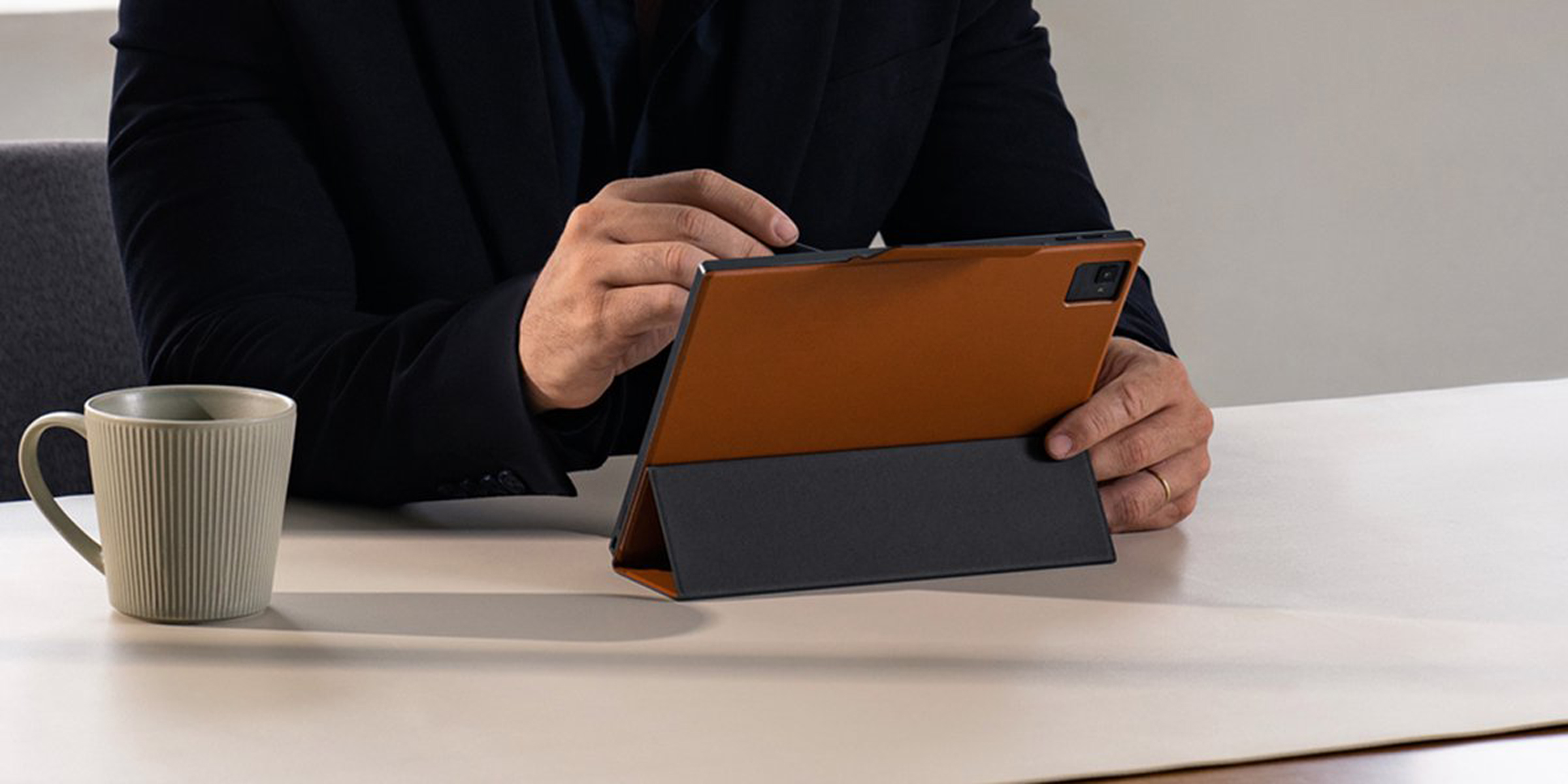 Eine Person benutzt ein Tablet mit einem Stift auf einem weißen Tisch, mit einer Kaffeetasse daneben.
