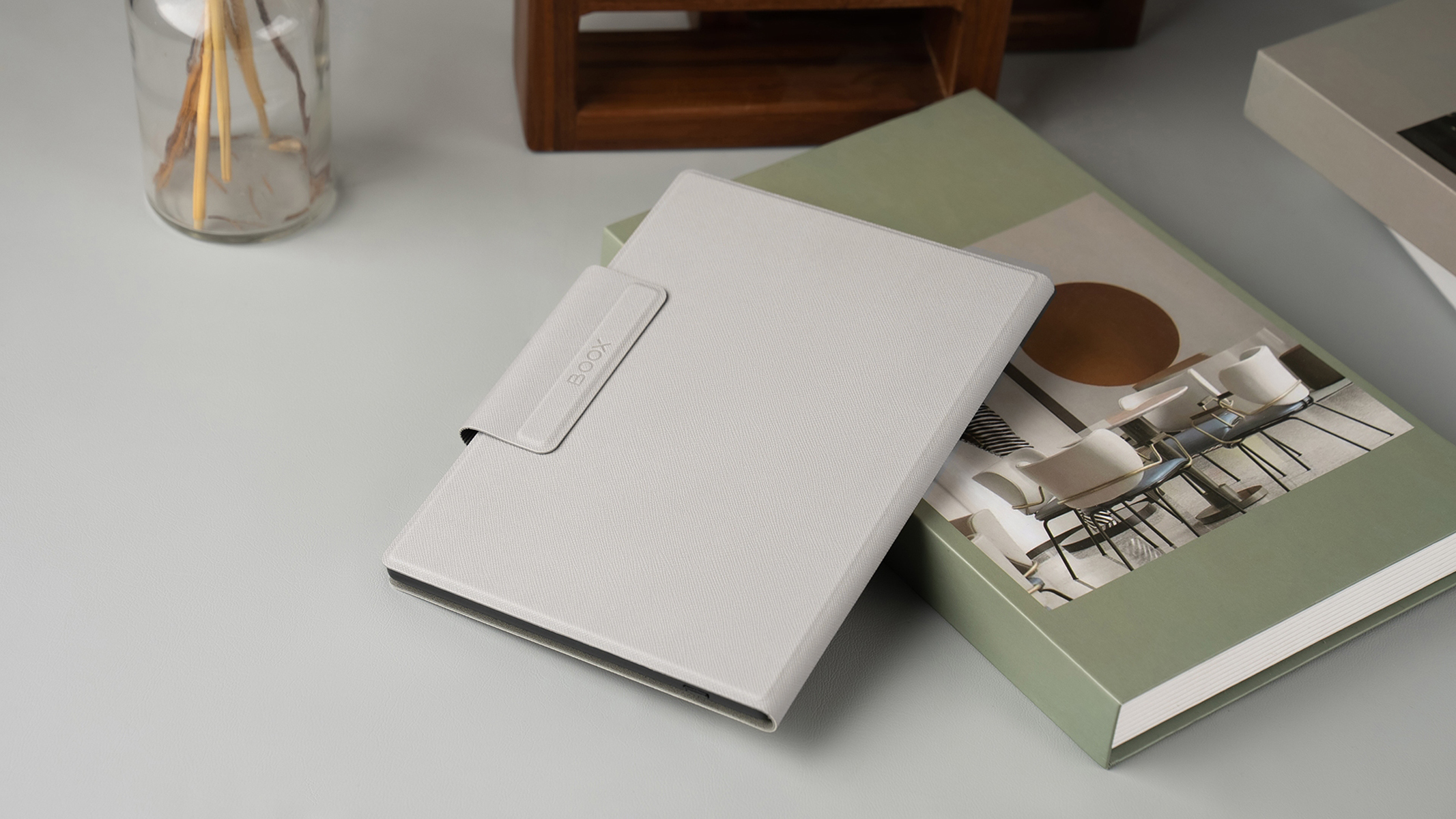 Tablet grigio chiaro con custodia su un libro verde e un tavolo. Decorazioni in legno sullo sfondo.