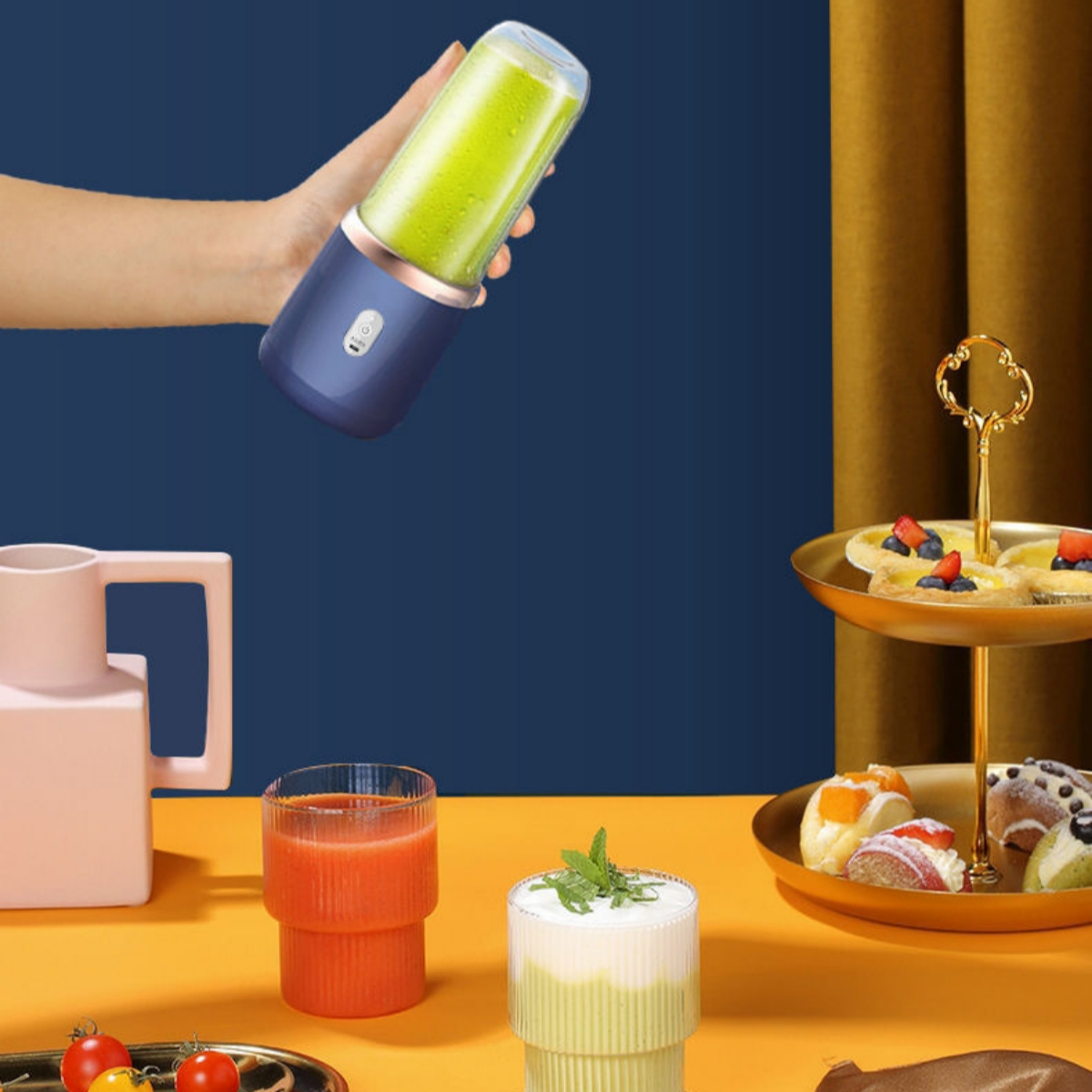 Hand hält Mixer mit grüner Flüssigkeit. Weitere Gläser und Tablett mit Essen. Blauer und gelber Hintergrund.
