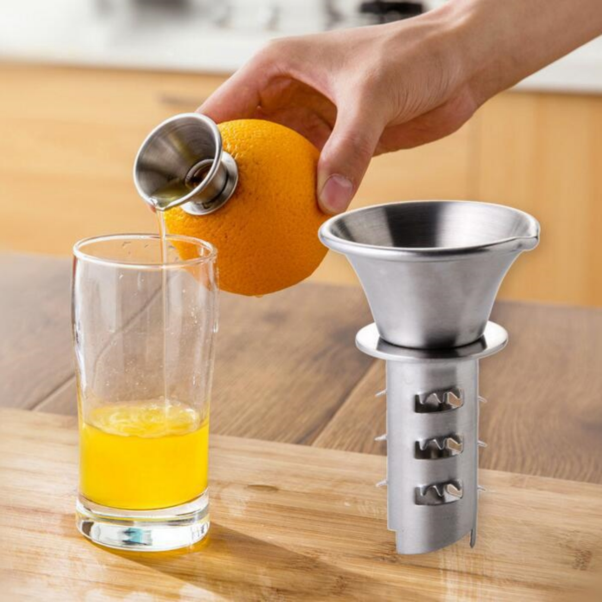 Eine Person gießt Saft aus einer Orange mit einer Saftpresse in ein Glas. Entsafter und Glas stehen auf einer Holzoberfläche.