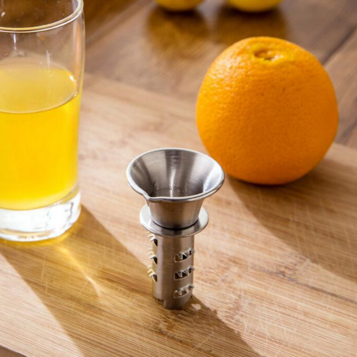 Eine Orange, ein Glas Saft und eine Zitruspresse aus Edelstahl auf einem Holzschneidebrett.