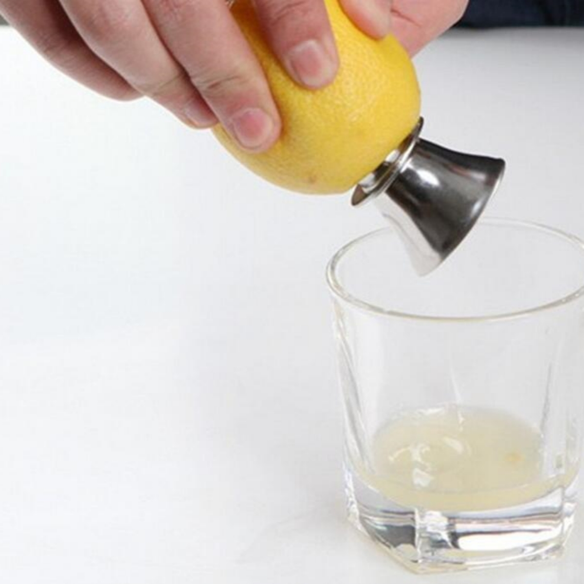 Hand presst Zitronensaft in ein Glas. Metall-Entsafter wird verwendet. Klare Flüssigkeit.