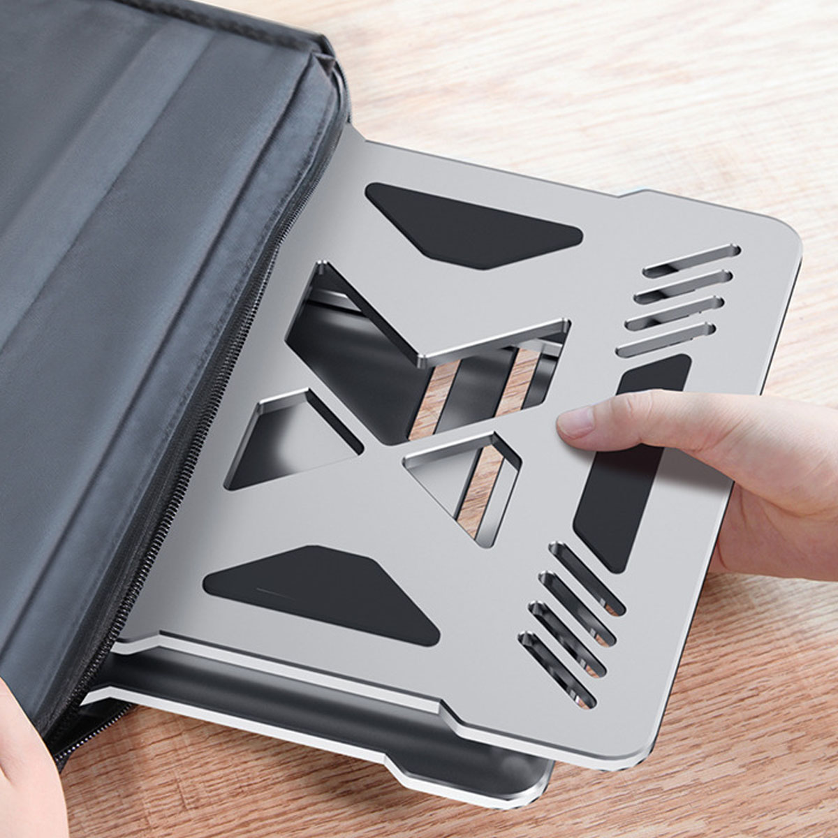 Ein silberner Laptop-Ständer, der von einer Hand aus einer grauen Tragetasche gezogen wird.