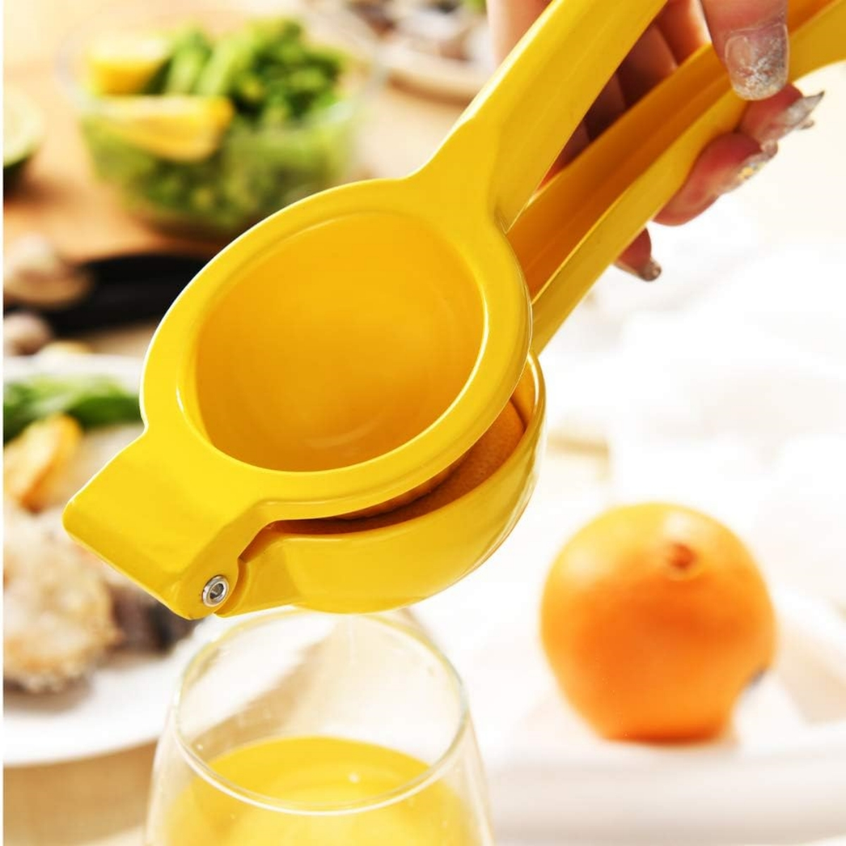Ein gelber Zitronenpresser presst eine Zitrone in ein Glas. Eine Orange ist in der Nähe.