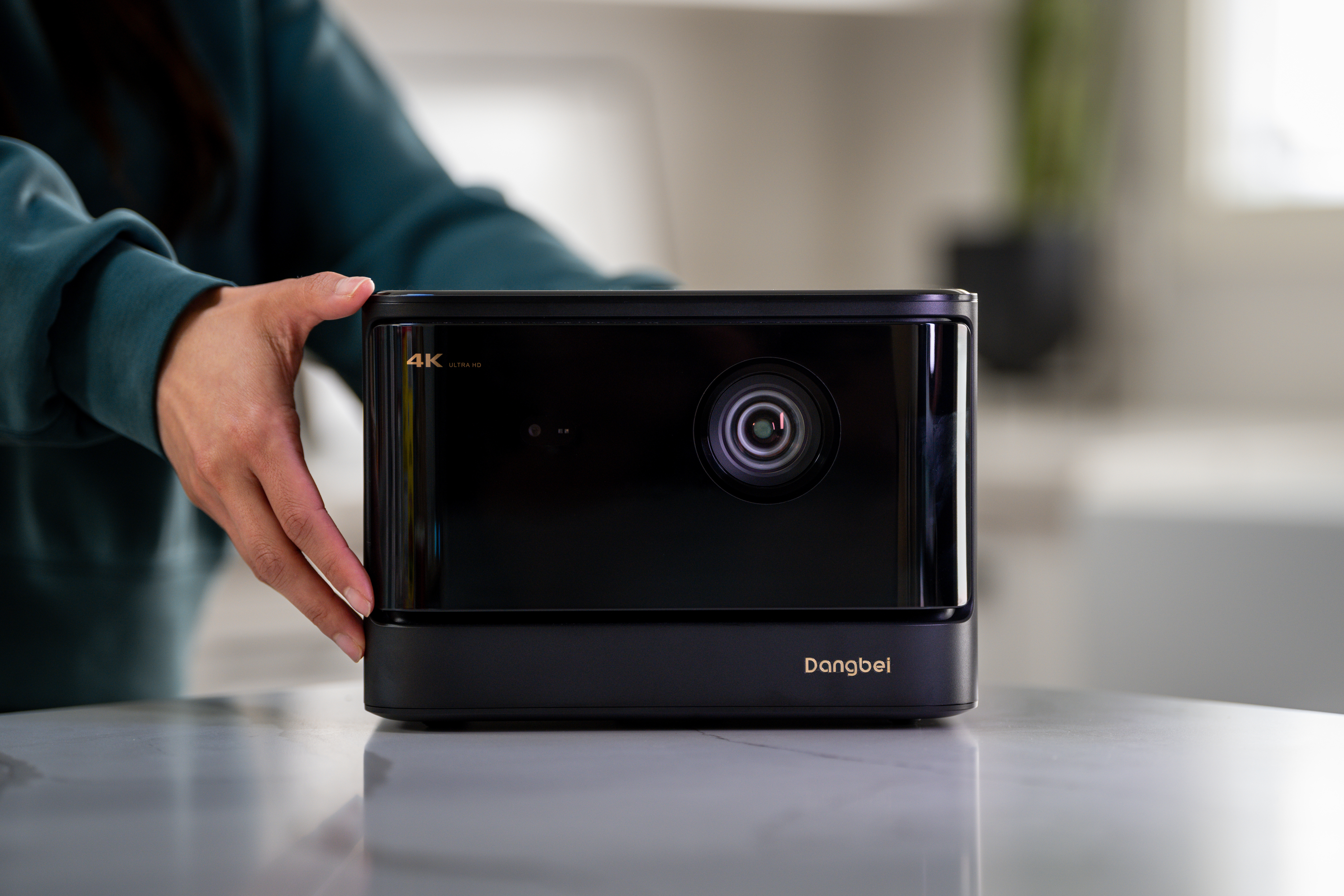 Czarny projektor trzymany przez osobę. Ma kilka etykiet i obiektyw.