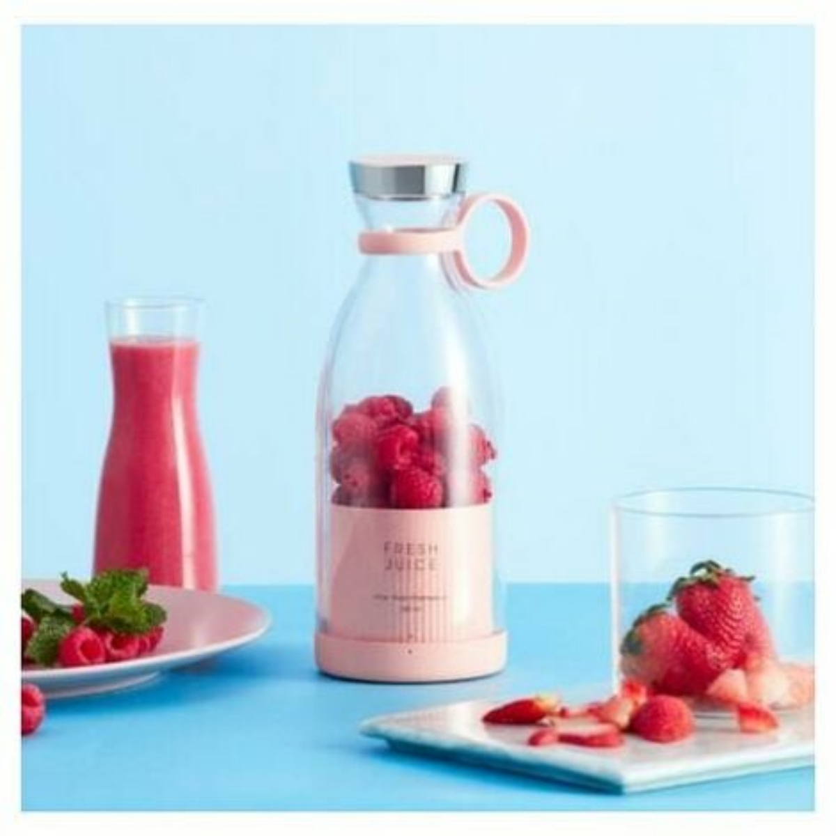 Pinkfarbener Mixer mit Himbeeren, Smoothie und Erdbeeren auf einem Teller. Blauer Hintergrund.