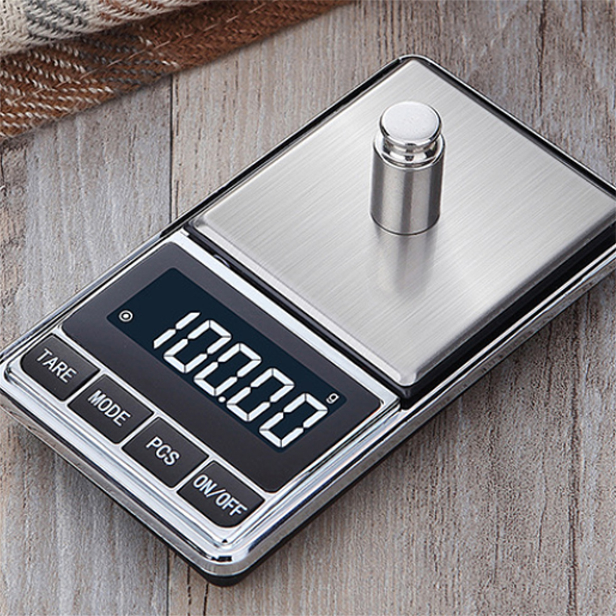Digitalwaage mit einem kleinen Gewicht darauf. Das Display zeigt 100,00 g an. Tasten sind beschriftet.