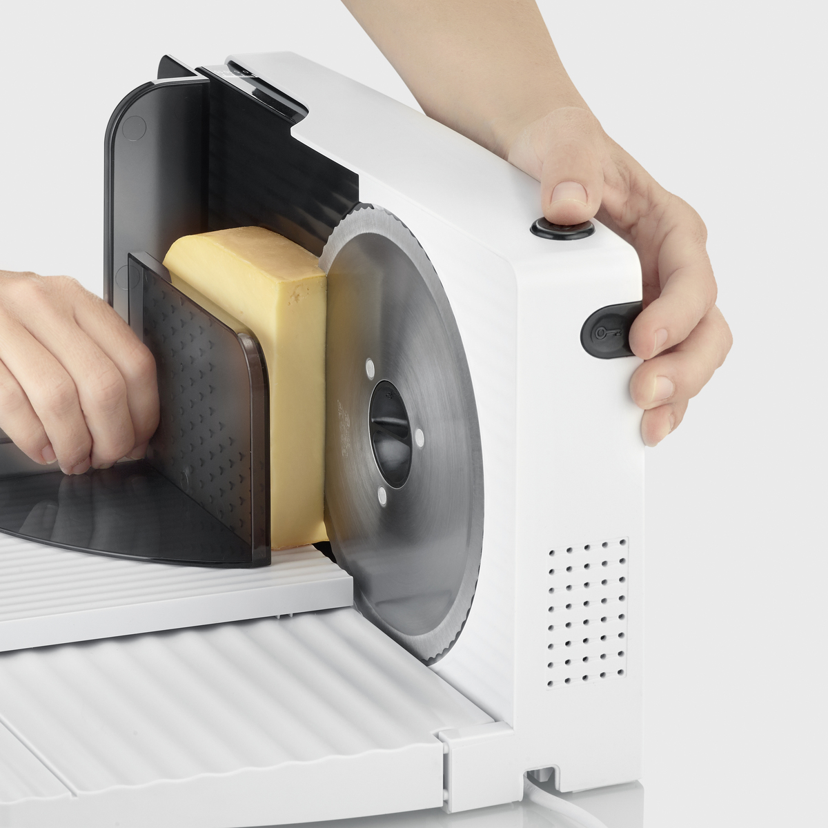 Osoba używa białej krajalnicy do sera z okrągłym ostrzem, krojąc żółty ser.