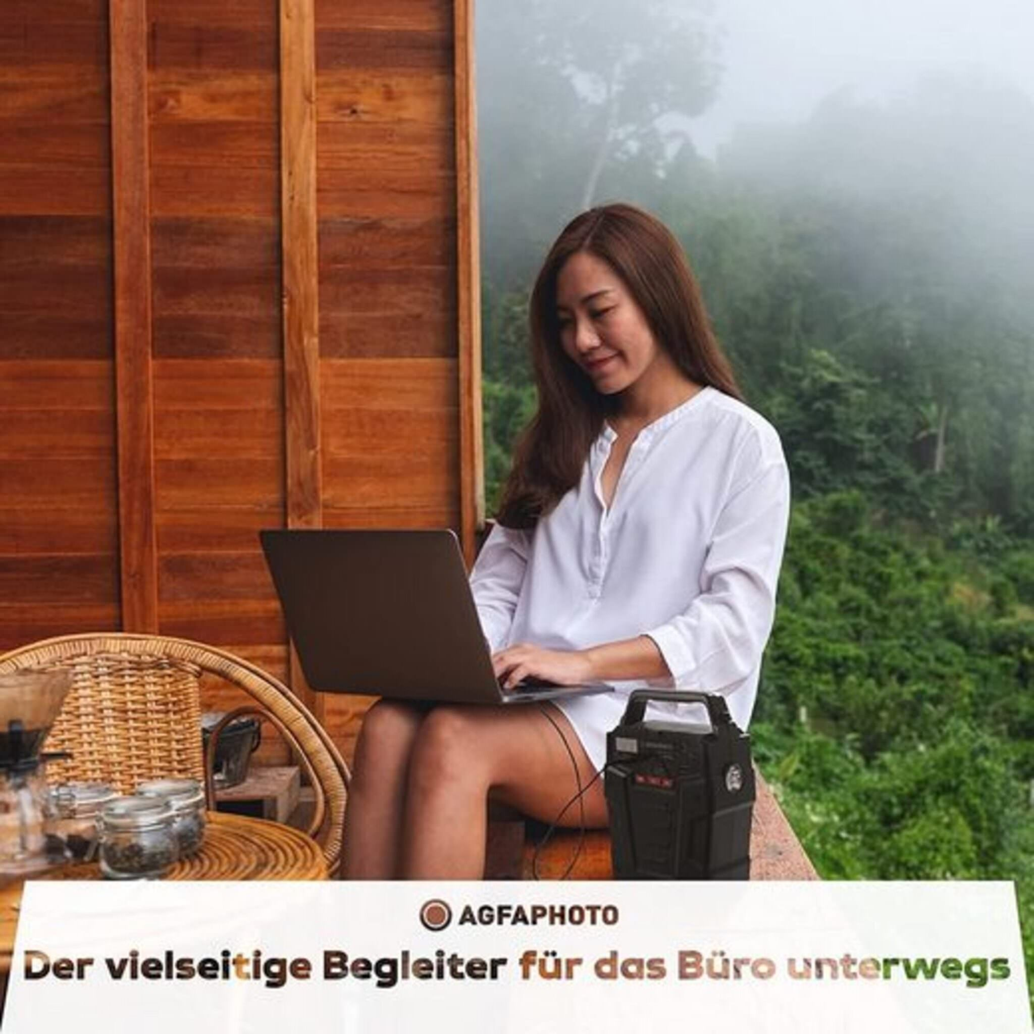 Frau benutzt Laptop auf Holzterrasse mit schwarzem Kraftwerk und Aussicht.