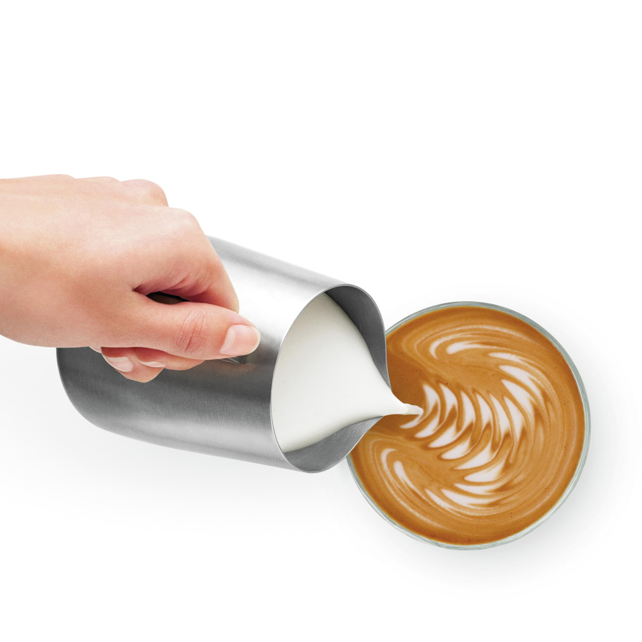 Ręka wlewa mleko do filiżanki kawy. Kawa ma latte art. Białe tło.