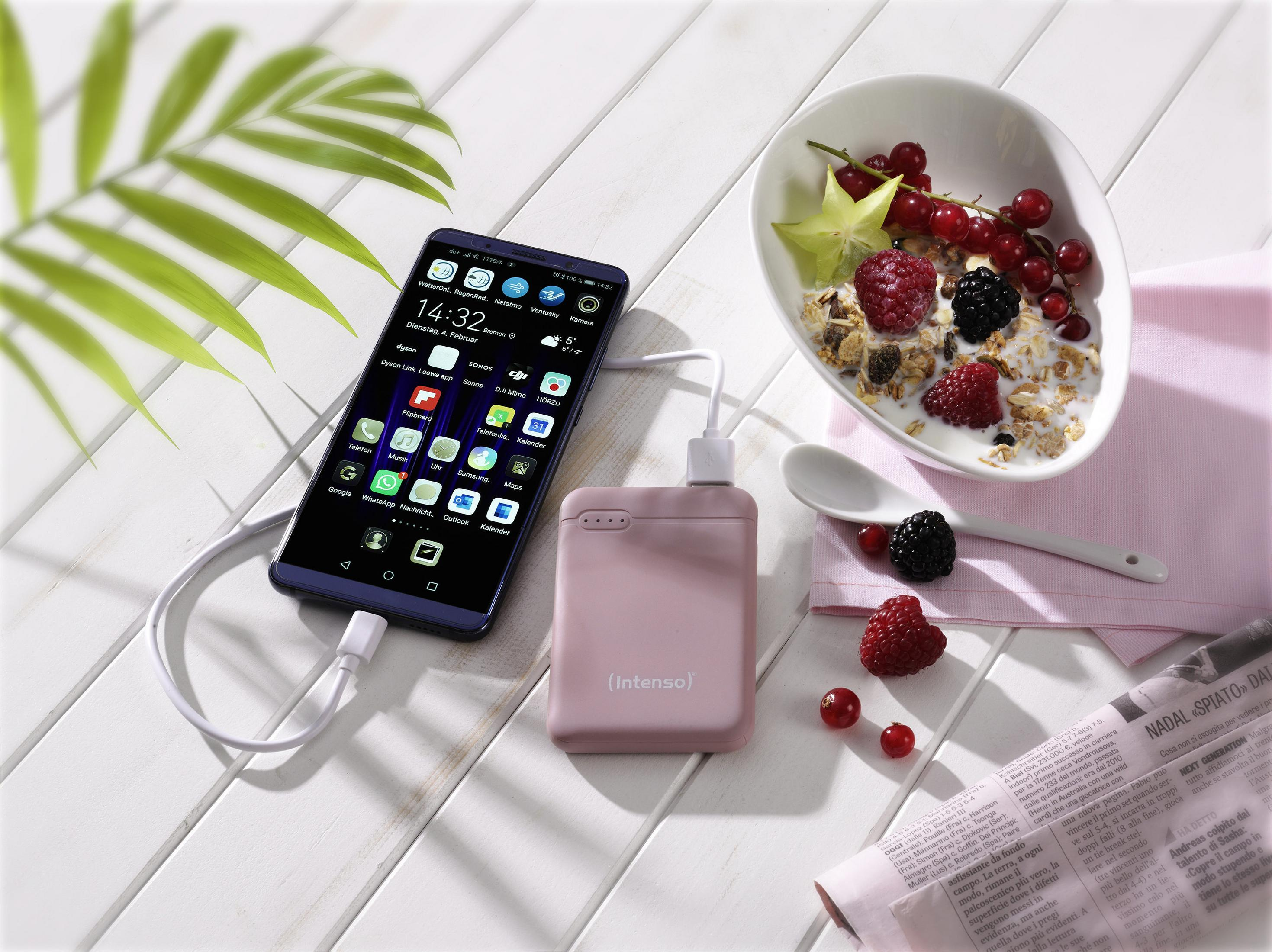 Telefon mit pinker Powerbank verbunden neben einer Schüssel Beeren und Joghurt.