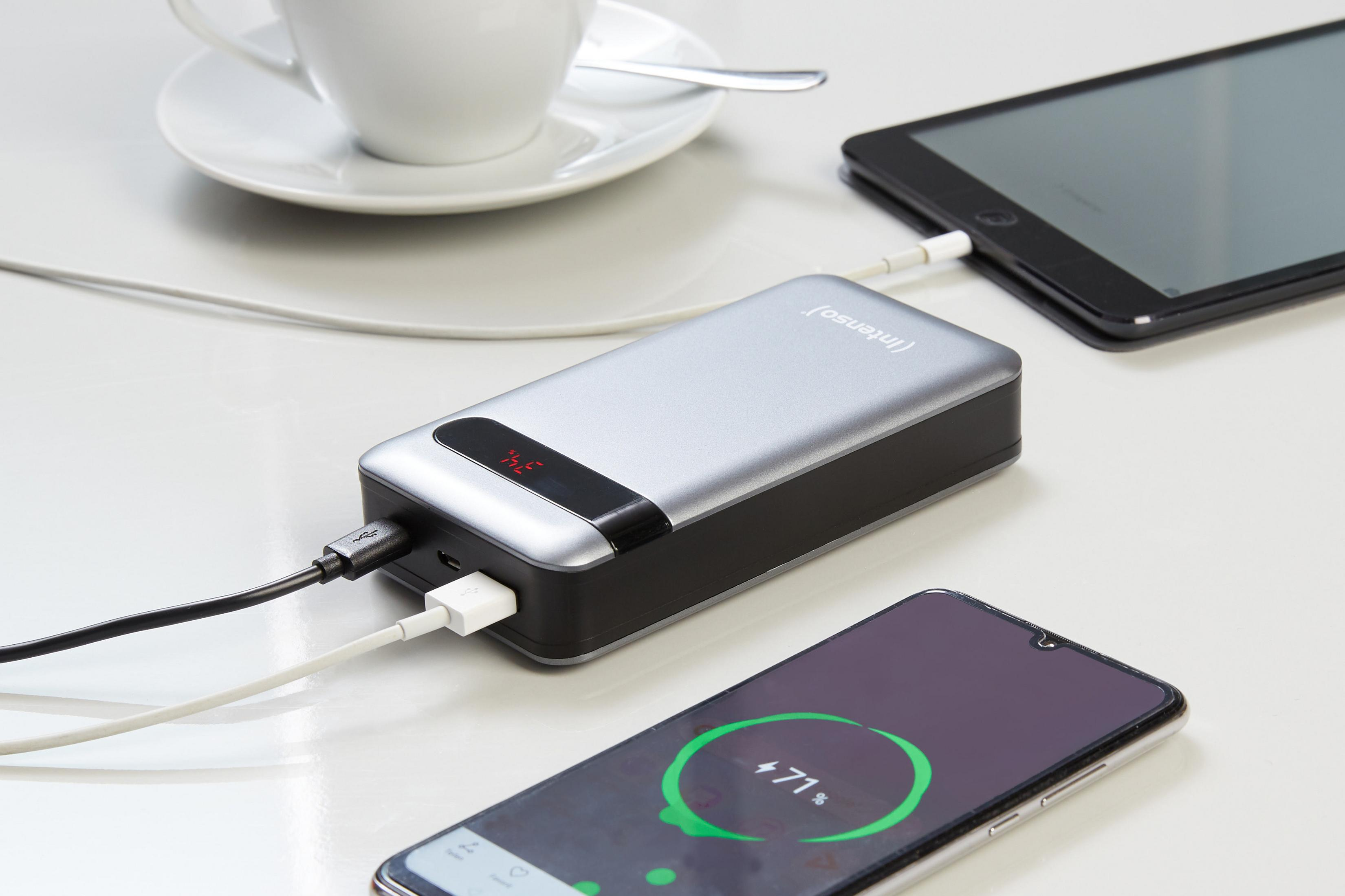 Een zilverkleurige powerbank die een telefoon en een tablet oplaadt op een wit oppervlak.