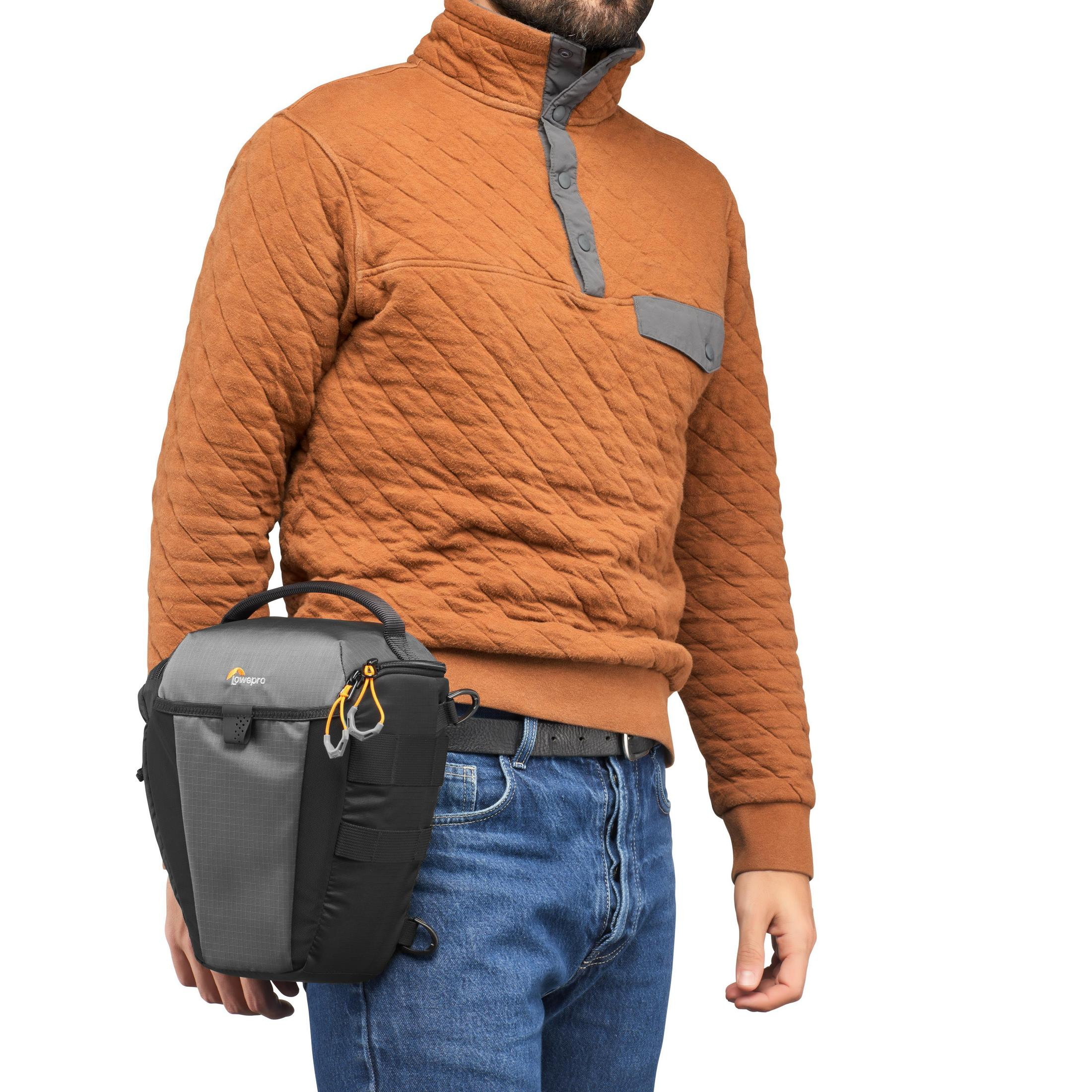Un homme portant un pull marron avec un sac d'appareil photo gris sur l'épaule.