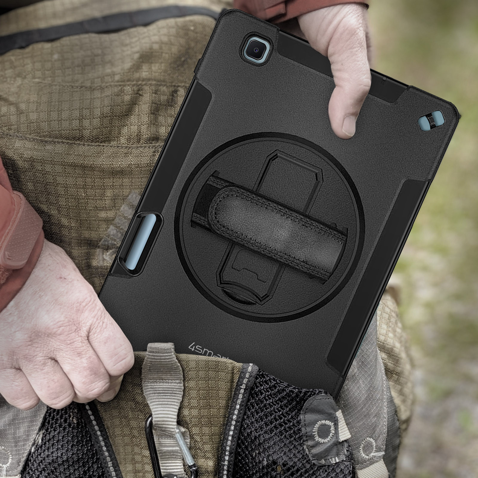 Eine Person hält ein schwarzes Tablet in einer schwarzen Hülle mit Handschlaufe vor einem Rucksack.