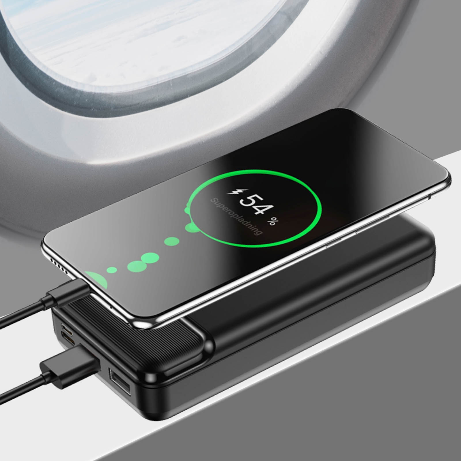 Schwarze Powerbank lädt Telefon mit 54 % Ladung. Flugzeugfenster im Hintergrund.